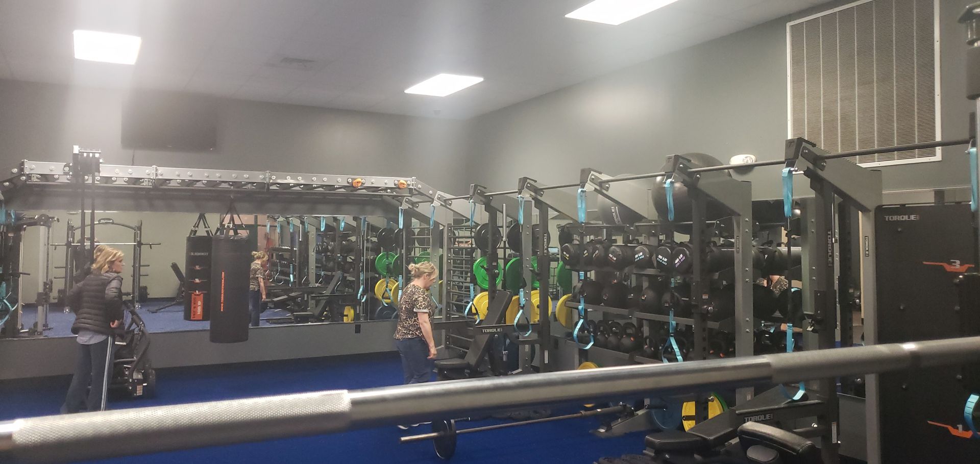 Gym with weight racks, exercise machines, and hanging straps under bright ceiling lights.