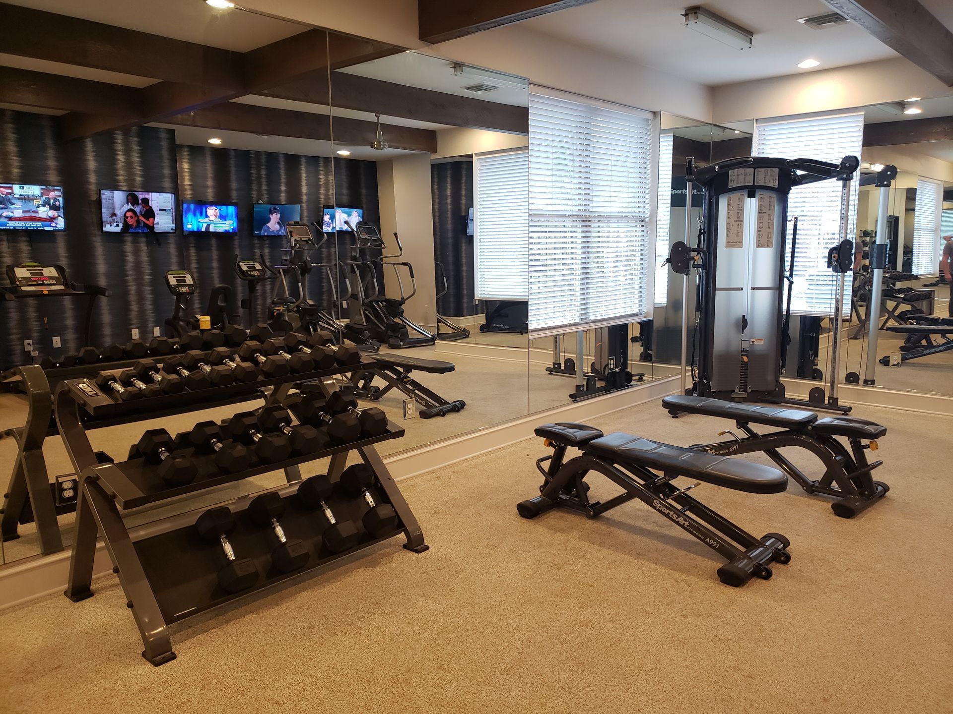 Gym with dumbbells, benches, and cable machines in a bright mirrored weight room