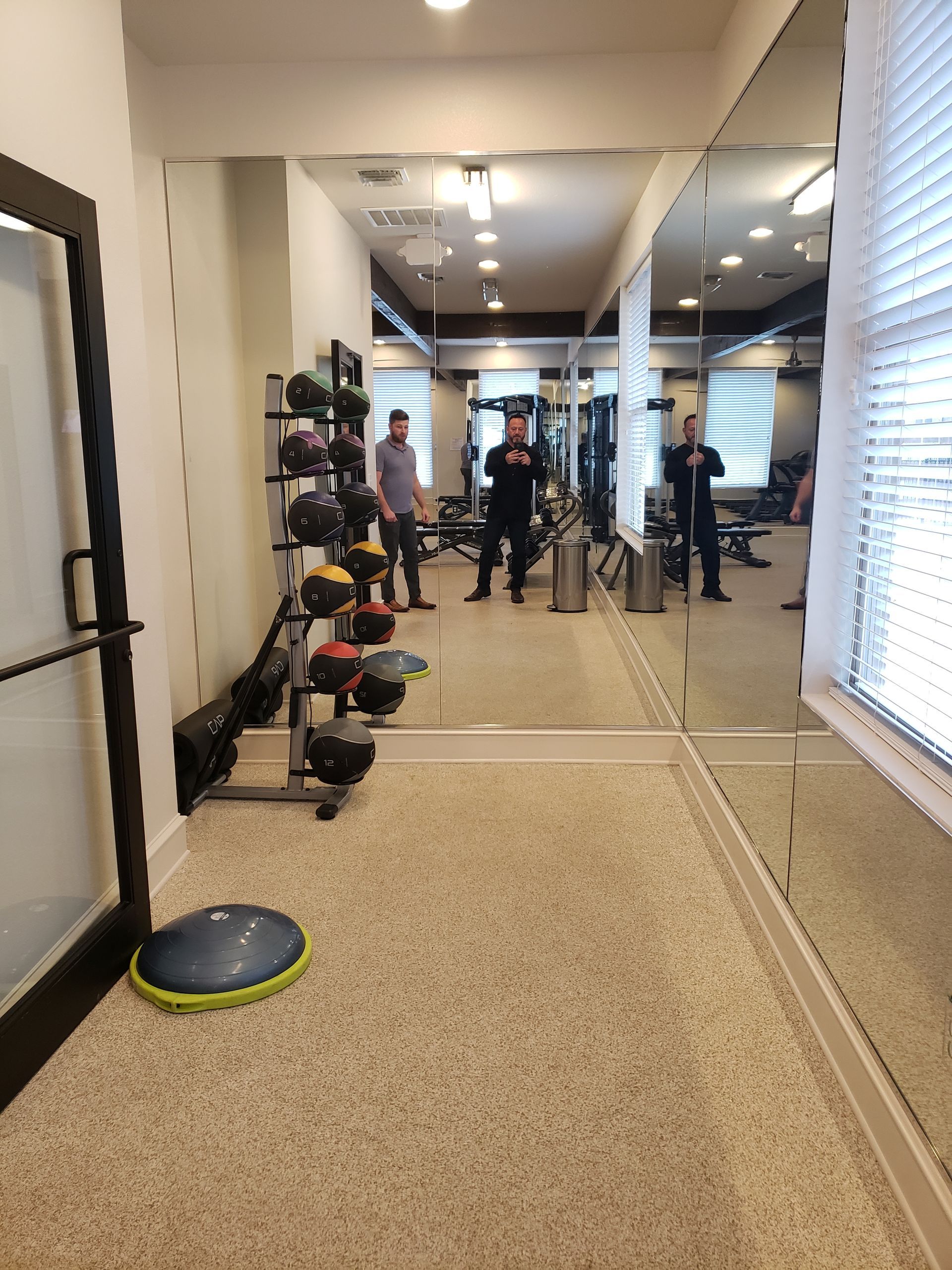 Gym studio with people exercising in front of mirrored walls and workout equipment.