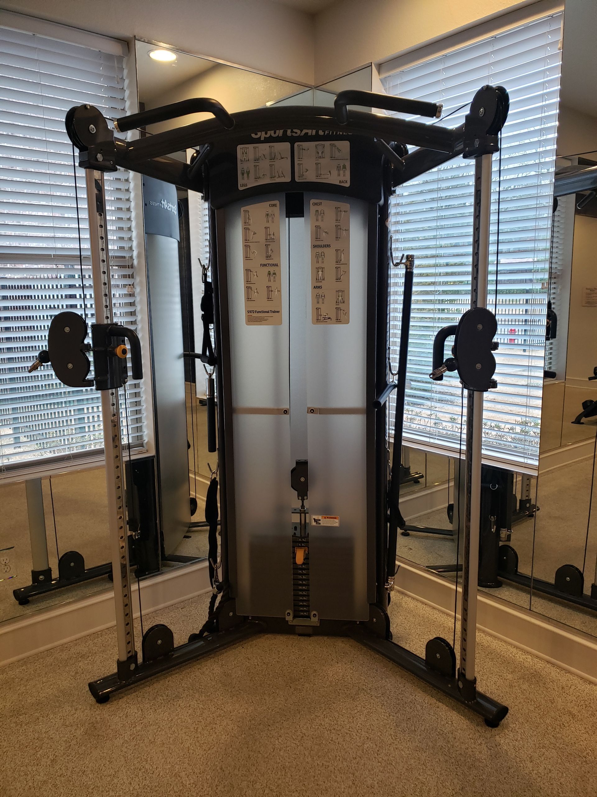 Gym cable machine in a room with large windows and blinds.