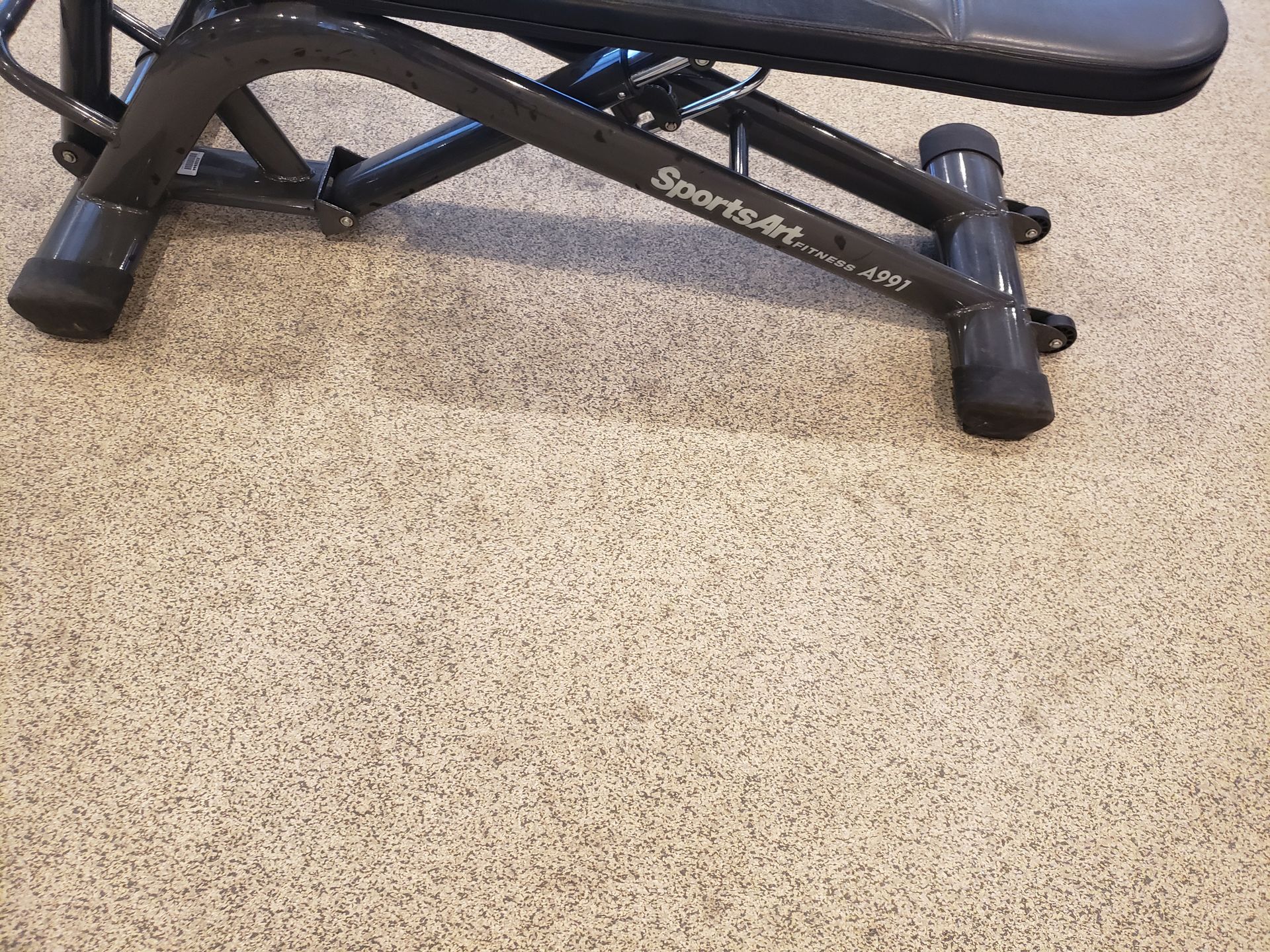Black exercise bench on beige floor, showing metal frame and padded seat.