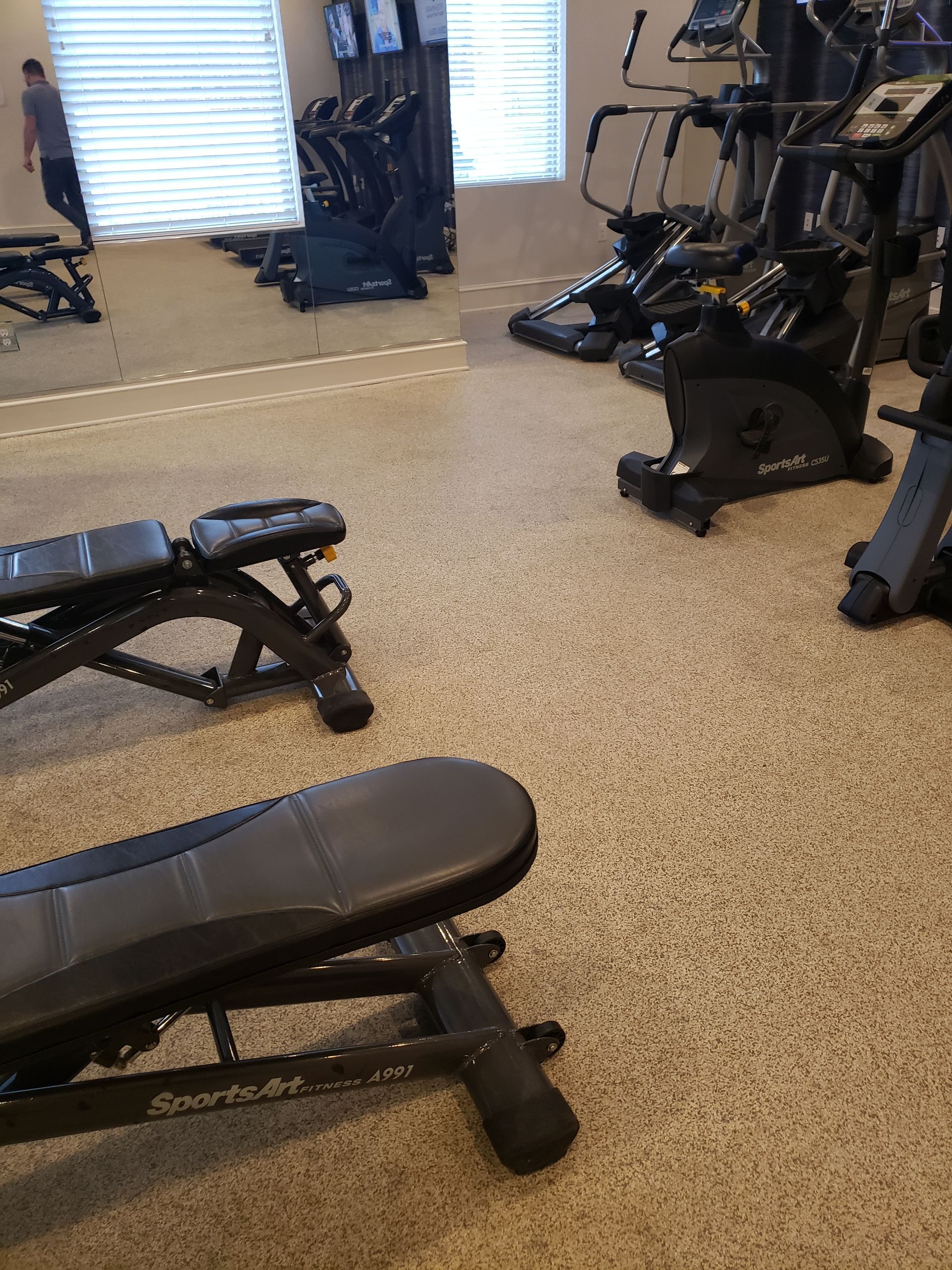 Gym room with black exercise benches and machines on a speckled floor.