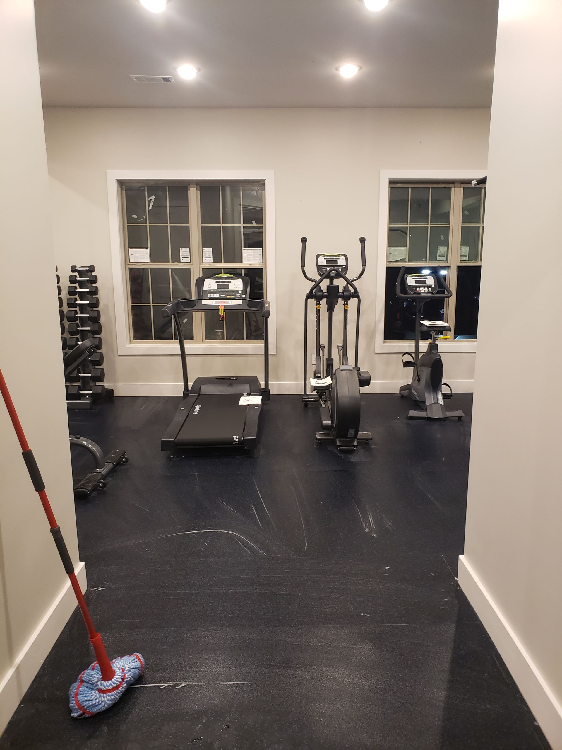 Small gym room with exercise machines, a treadmill, and a mop on the floor