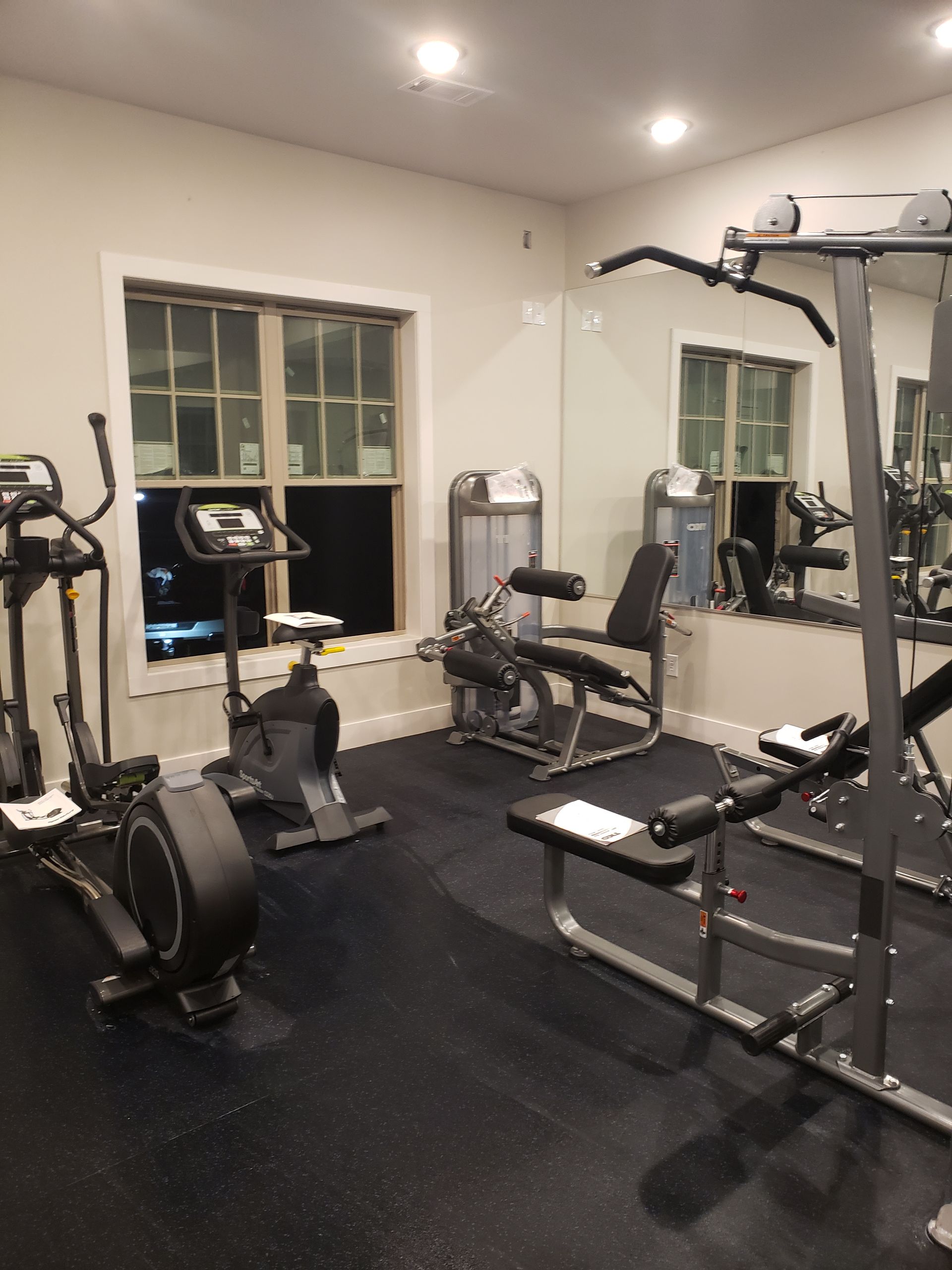 Small gym with black equipment, weights, mirror, window, and cable machine on a black floor.