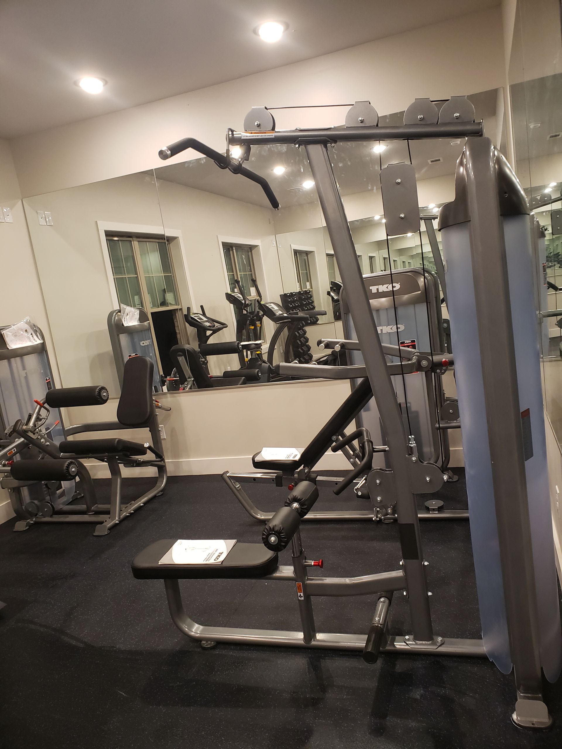 Compact gym with cable machine, bench, and mirrors in a carpeted room.