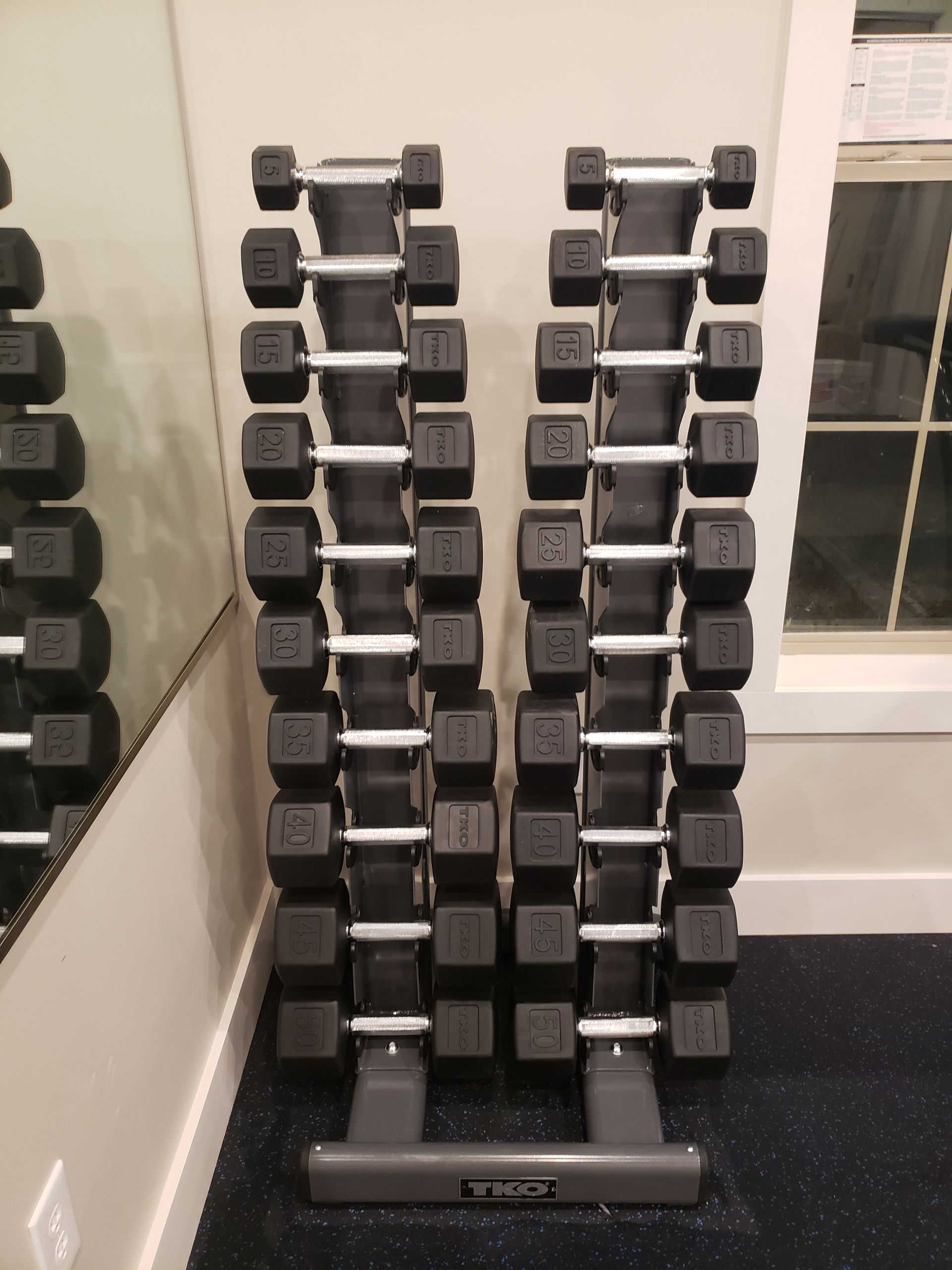 Vertical dumbbell rack with black and silver dumbbells in a gym near a wall and door