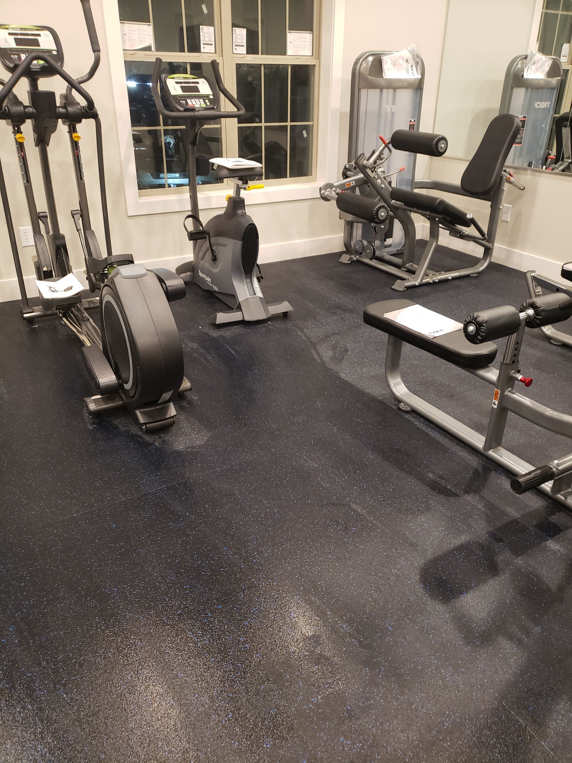 Small gym with exercise bikes, weight machines, and black rubber flooring.