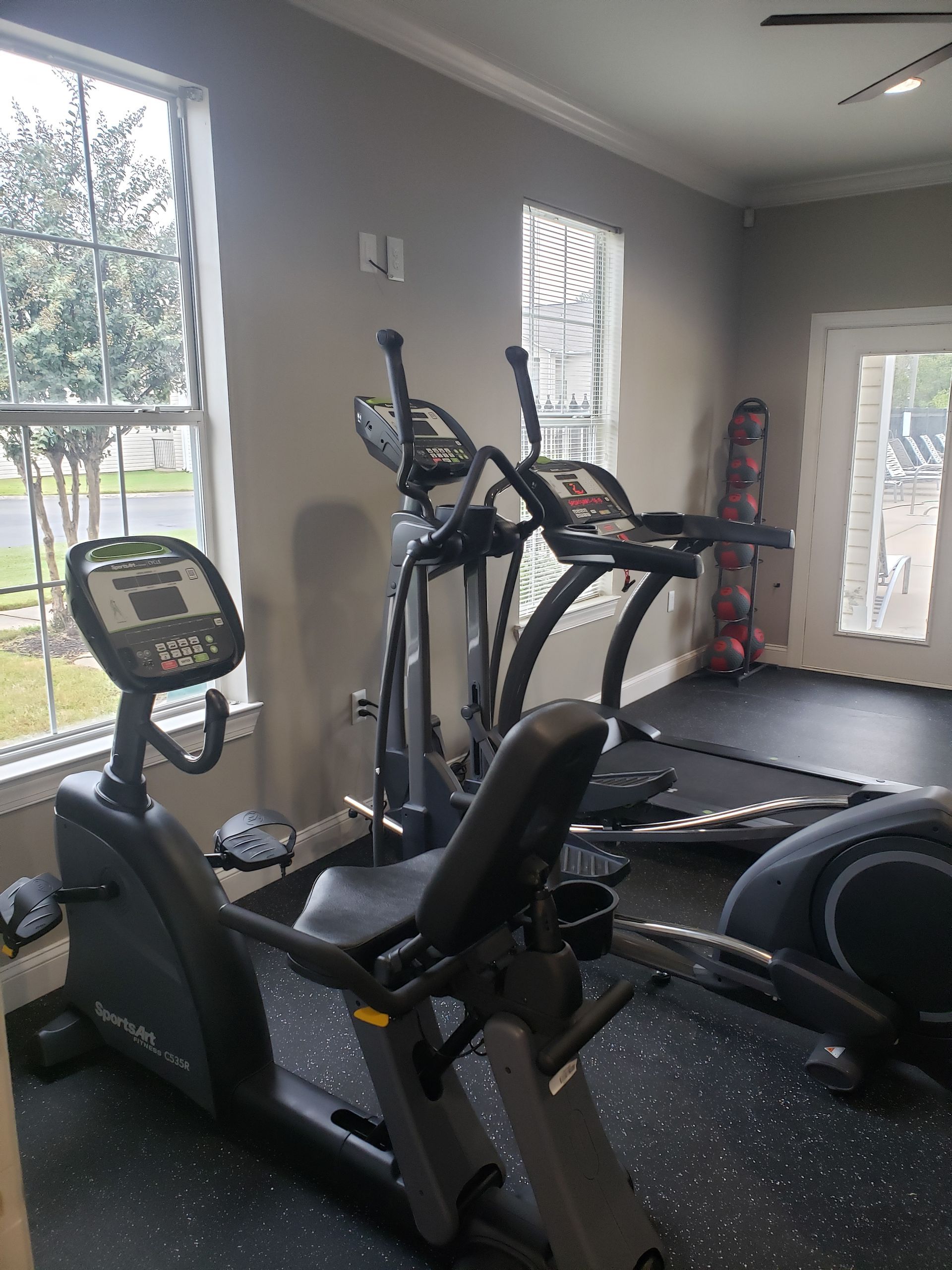 Gym with exercise bike, elliptical, and treadmill in a room with gray walls and large windows