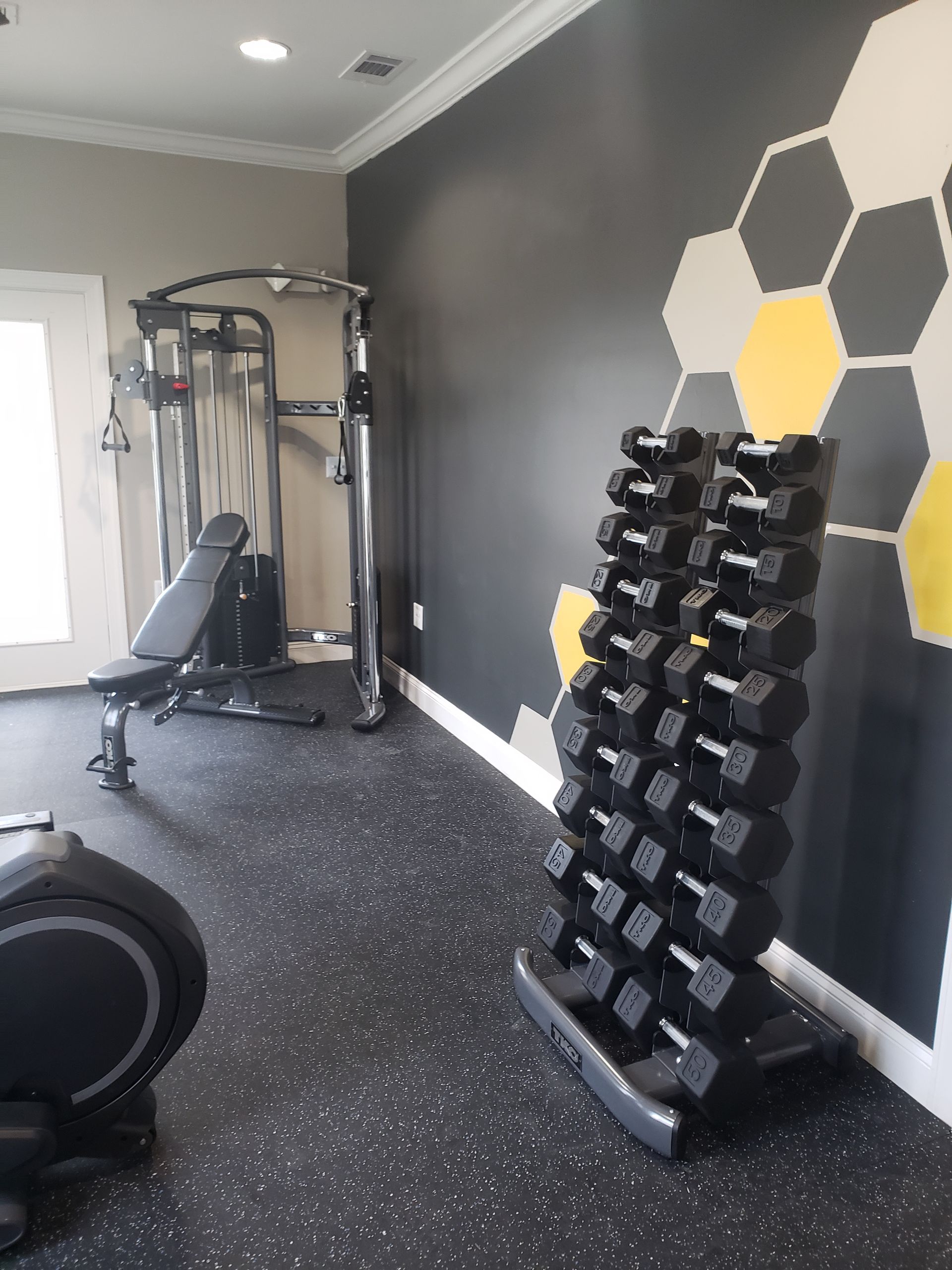 Gym with cable machine, dumbbell rack, and gray walls with yellow hexagon accents.