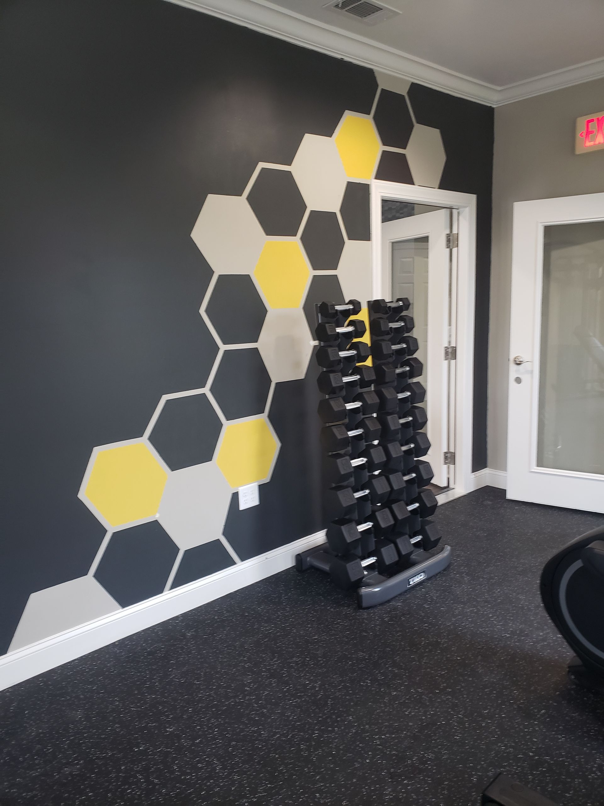 Gym interior with hexagon wall mural and a rack of dumbbells on black rubber flooring
