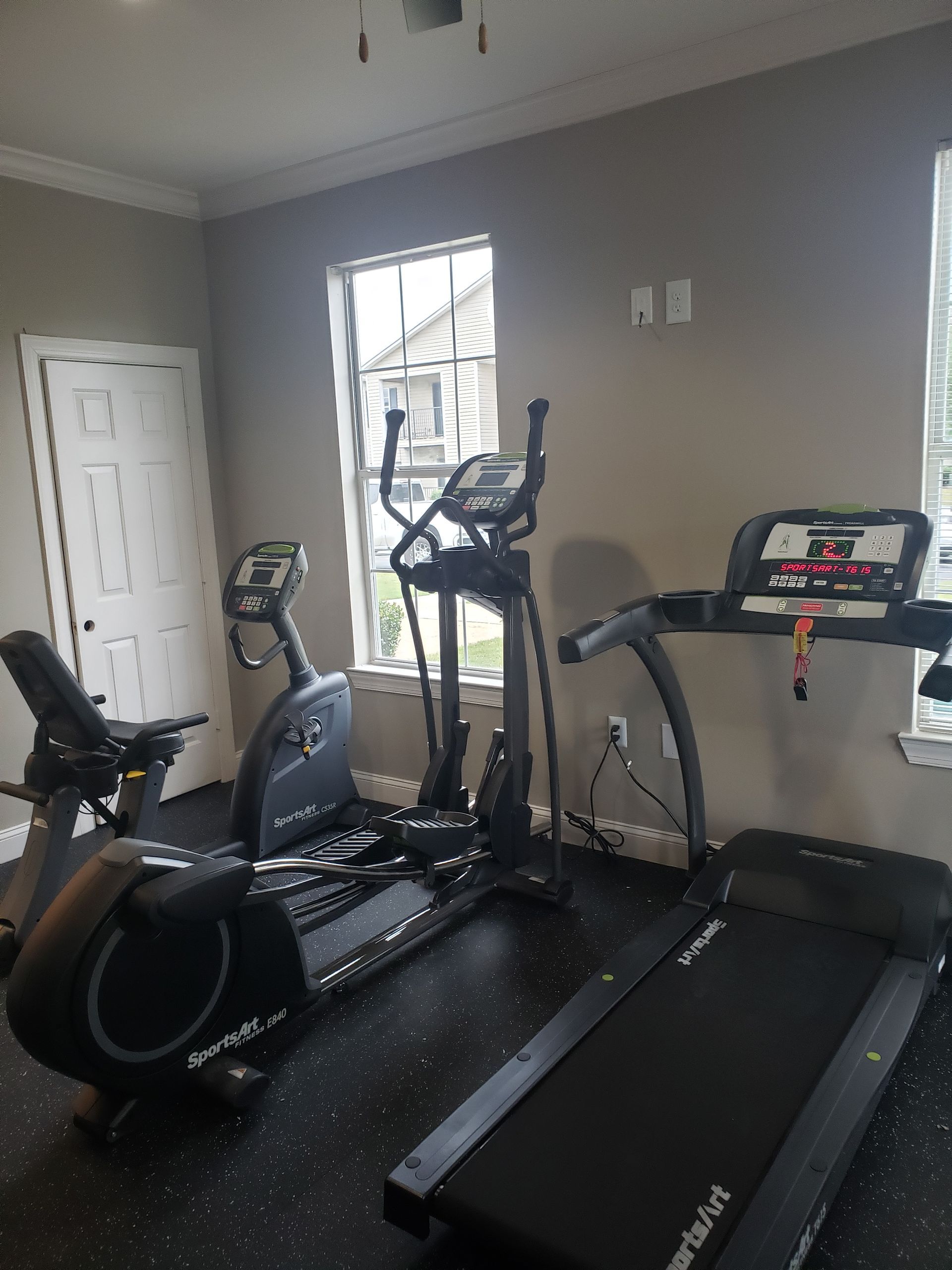 Gym with black elliptical, exercise bike, and treadmill in a gray room with a window and door.