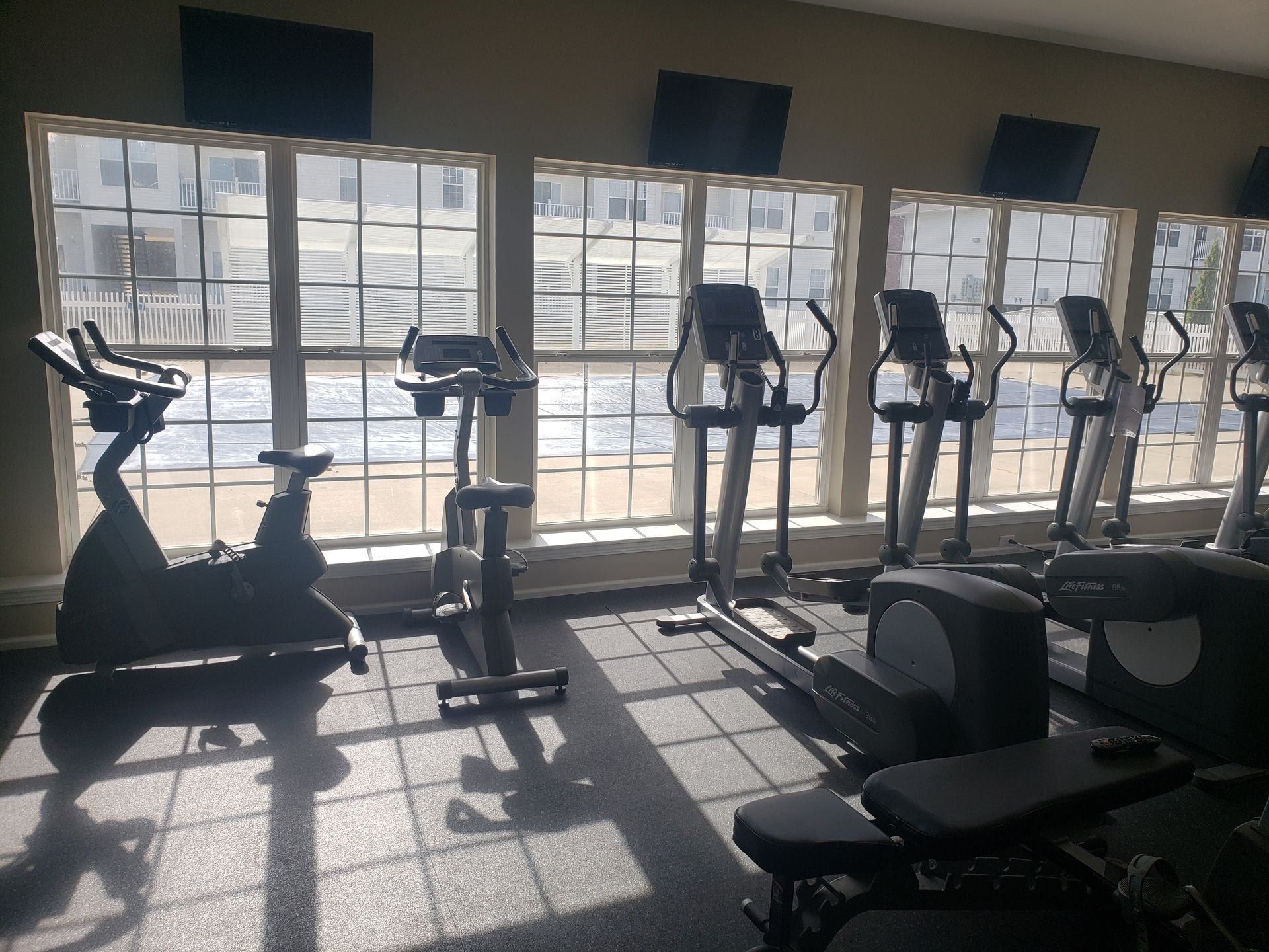 Gym cardio area with treadmills and stationary bikes by large sunlit windows