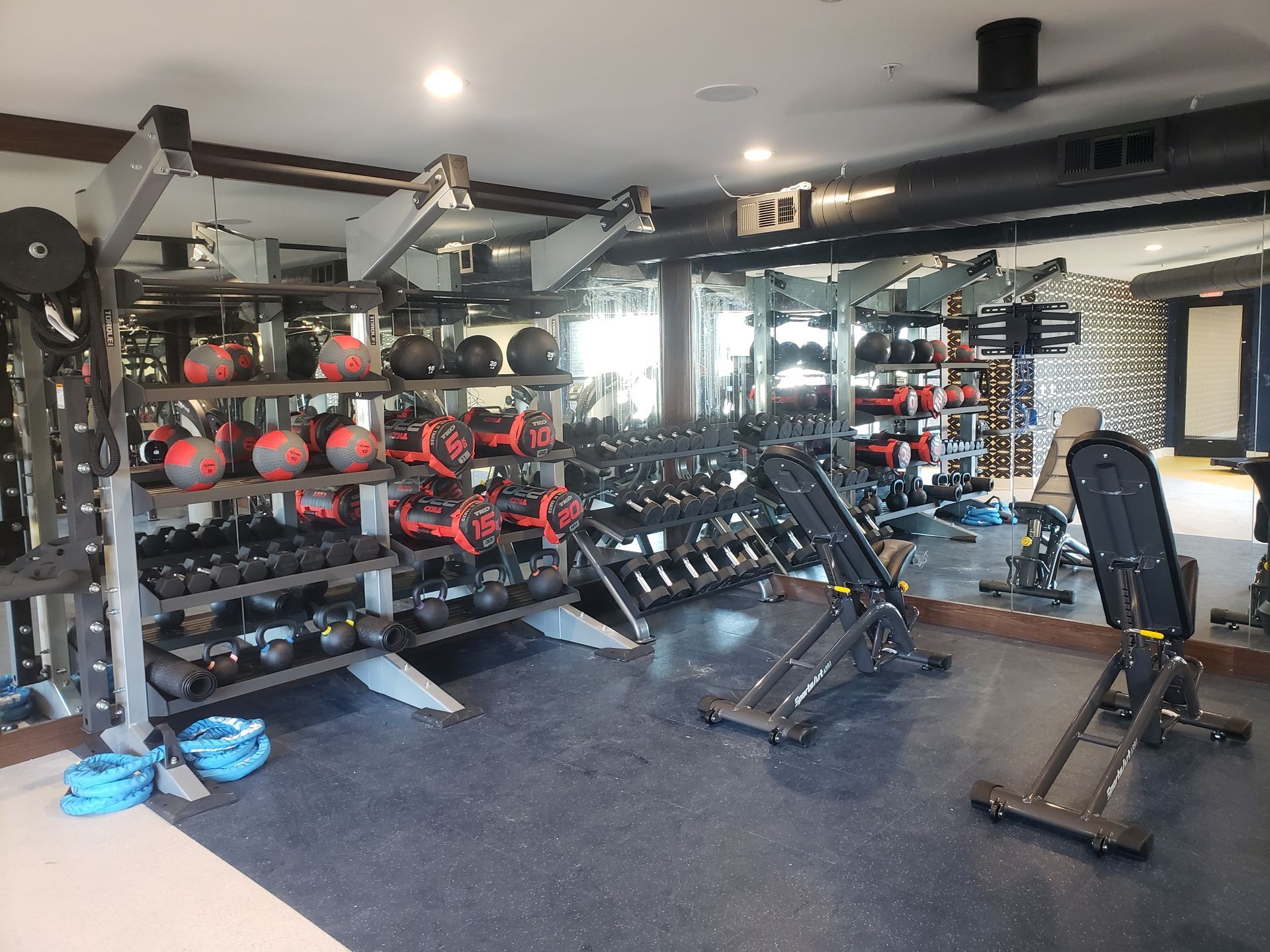 A gym room with weight racks, benches, barbells, and exercise equipment on a black floor.