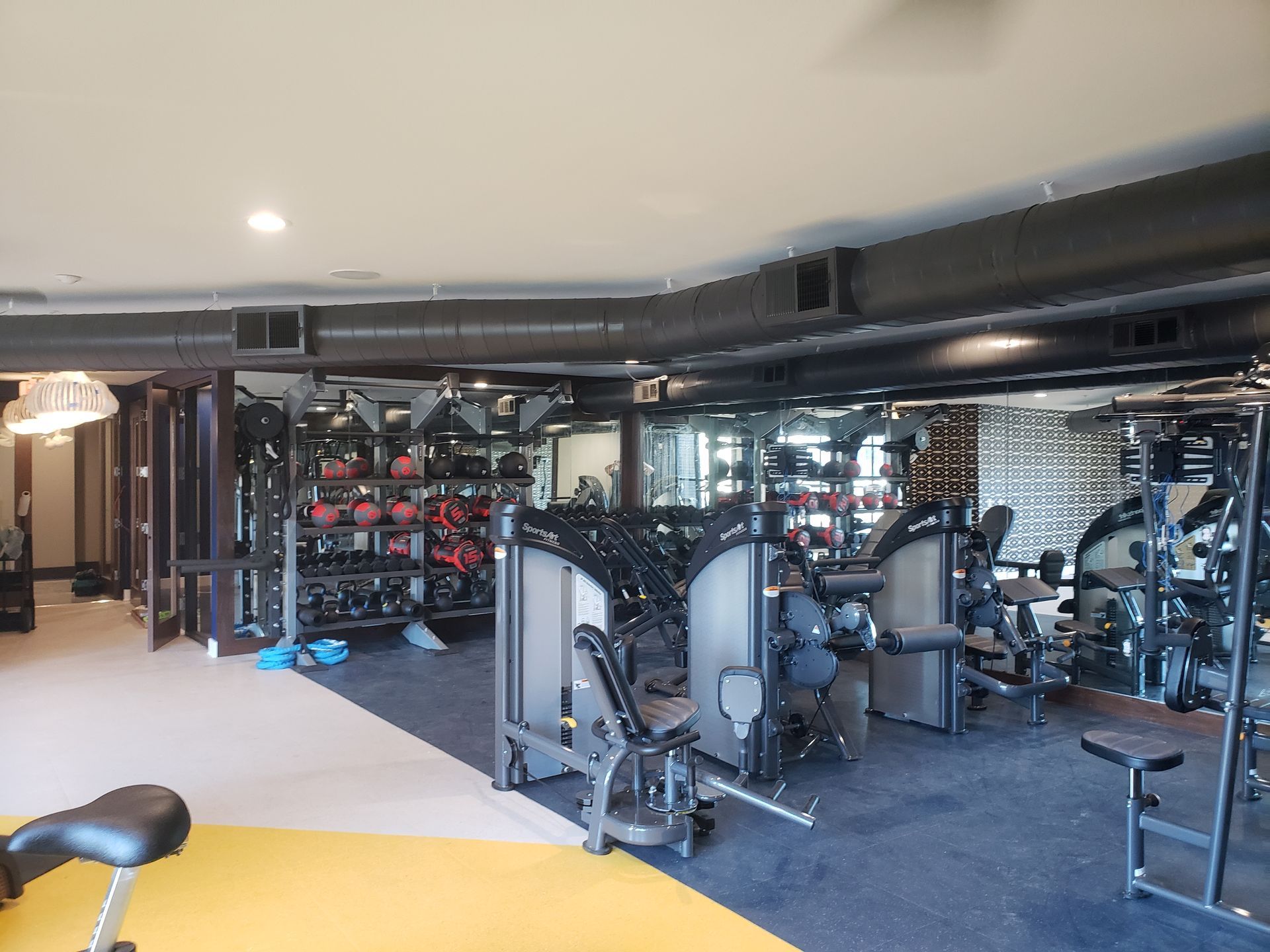 Modern gym interior with cardio and weight machines, mirrors, and black and gray equipment