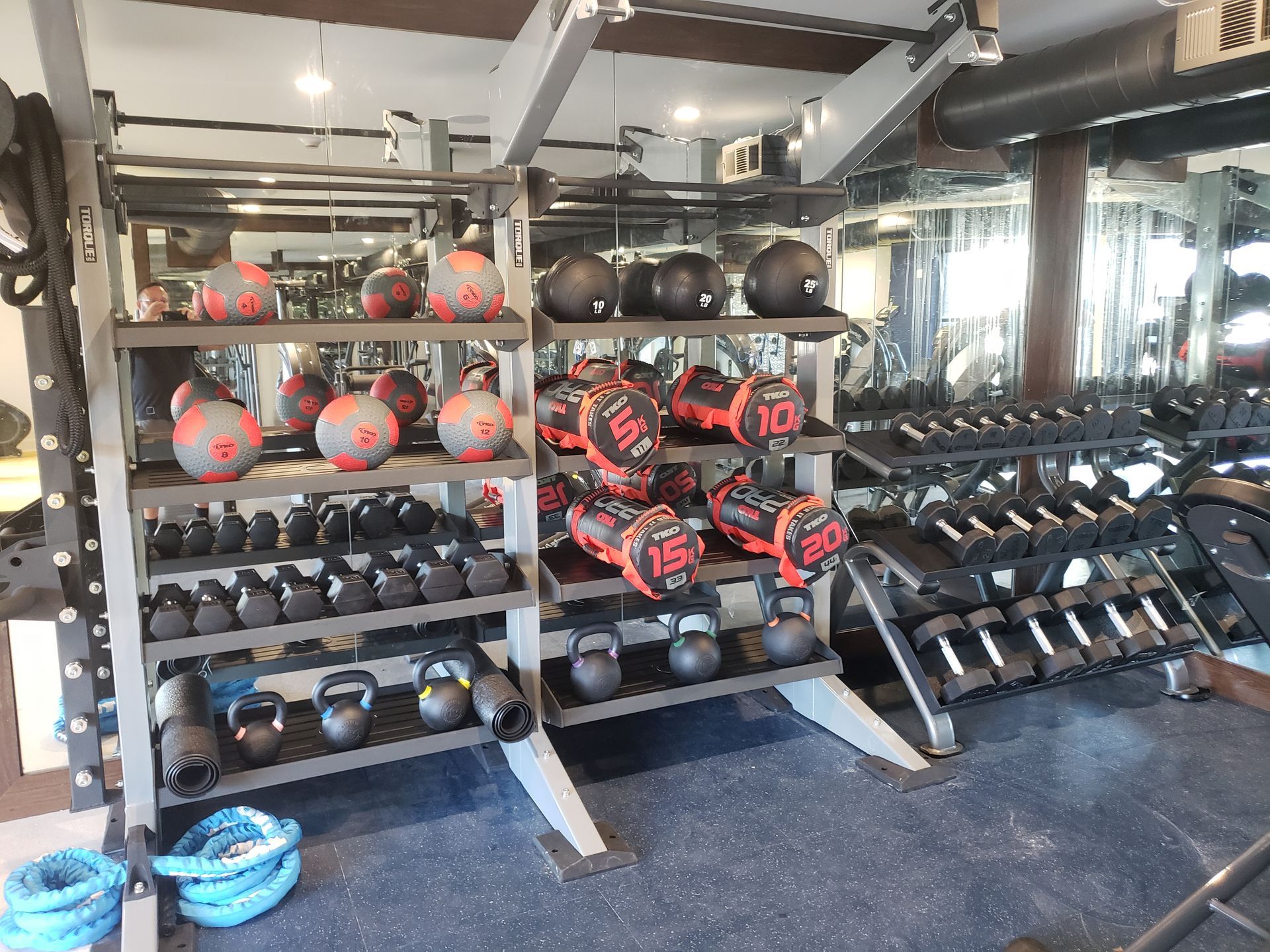 Gym weight rack with dumbbells, kettlebells, medicine balls, and red-black training balls in a workout room