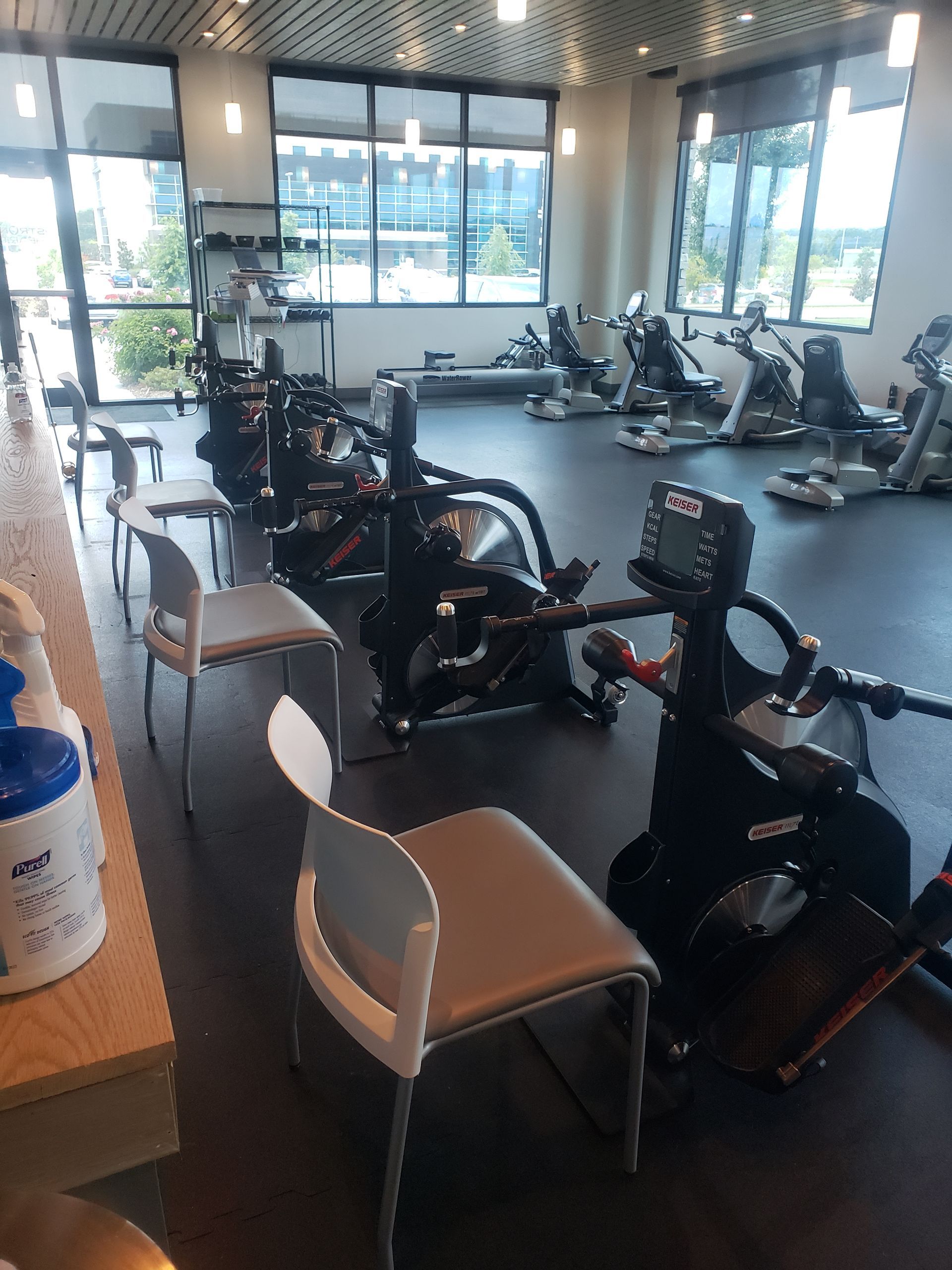 Gym with several stationary bikes and chairs near large windows.
