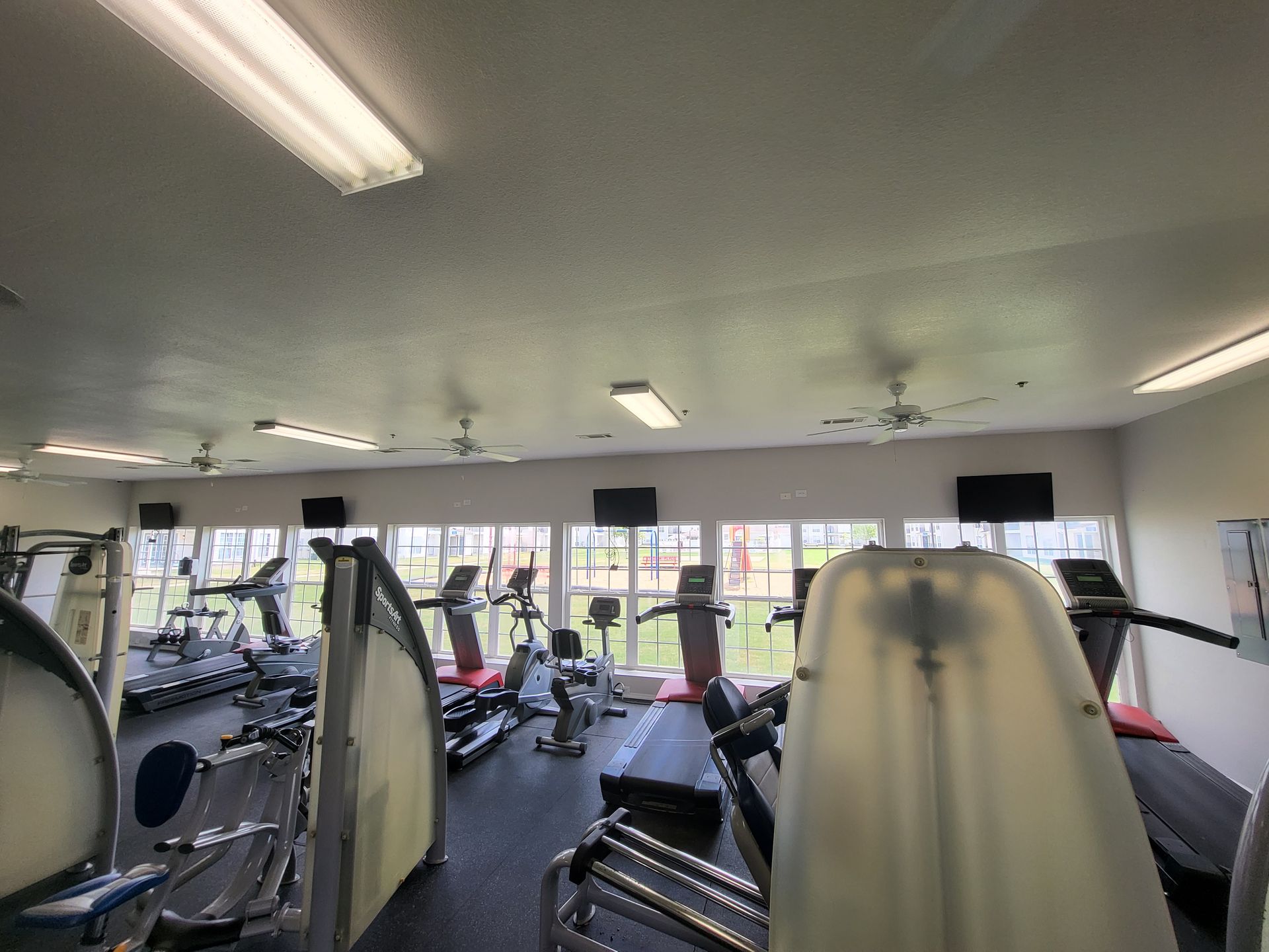 Gym interior with exercise machines, treadmills, and large windows along the wall.