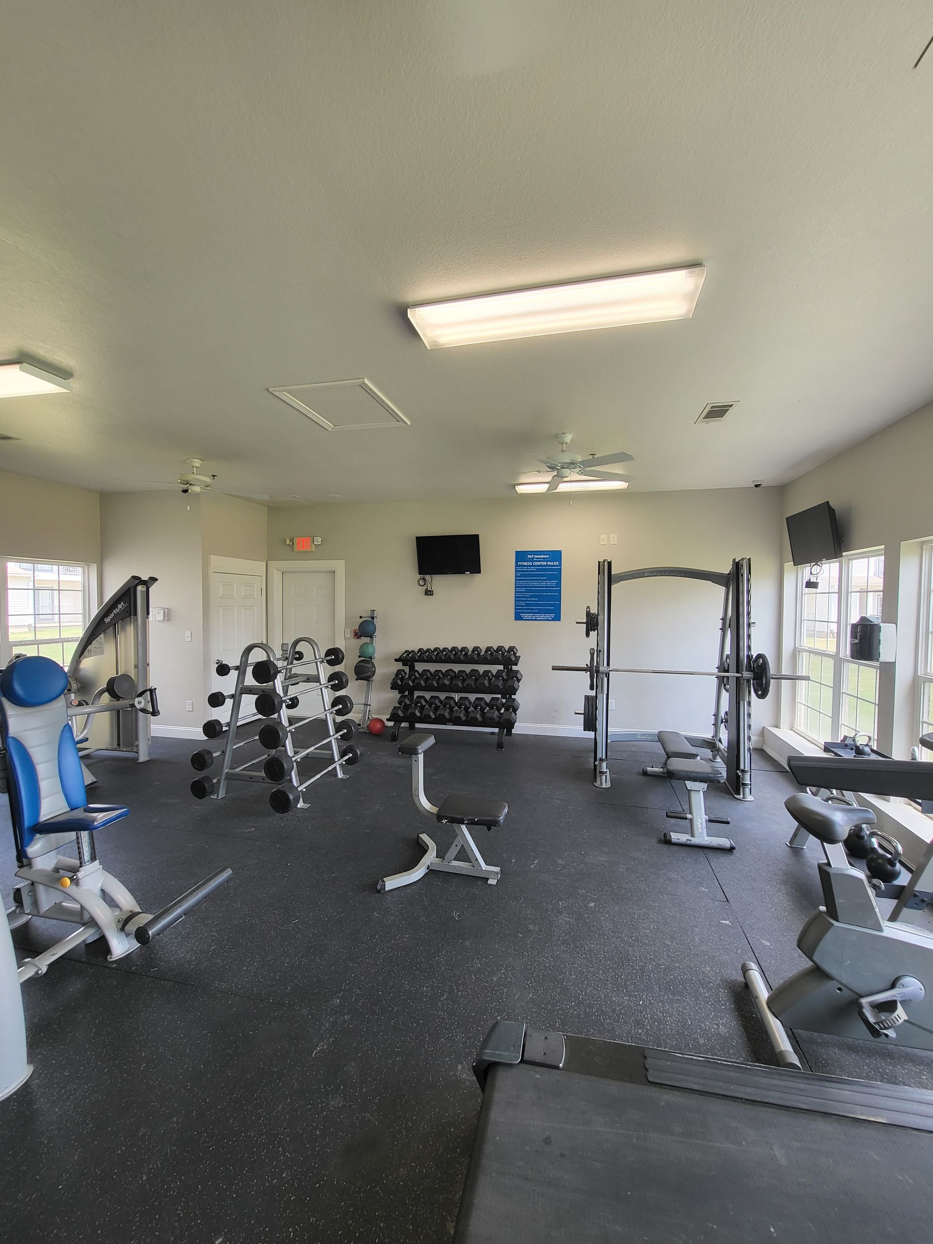 Gym interior with weight machines, dumbbells, benches, and black rubber flooring under bright ceiling lights