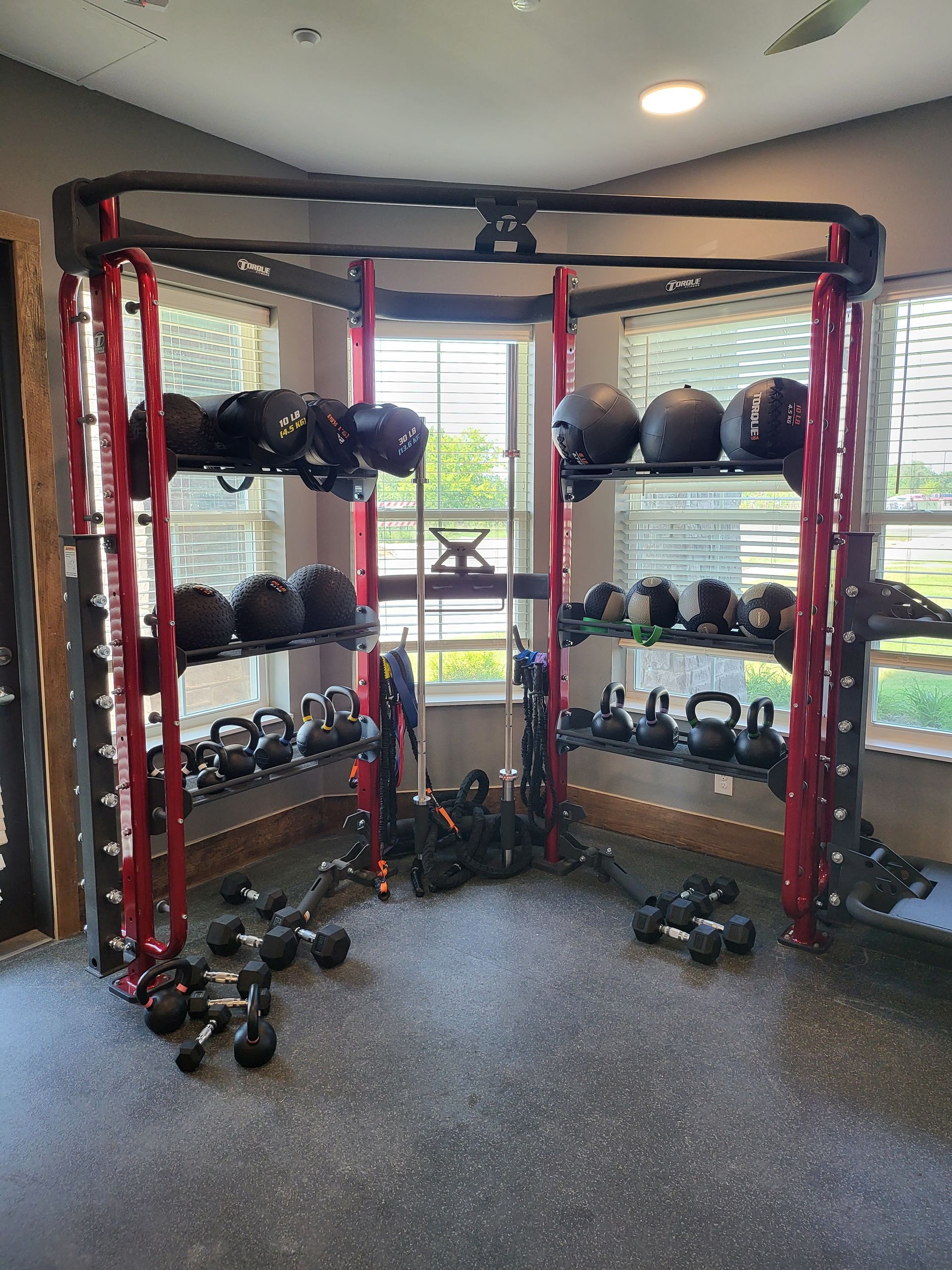 Compact gym corner with red rack, shelves of kettlebells and medicine balls, and dumbbells on the floor