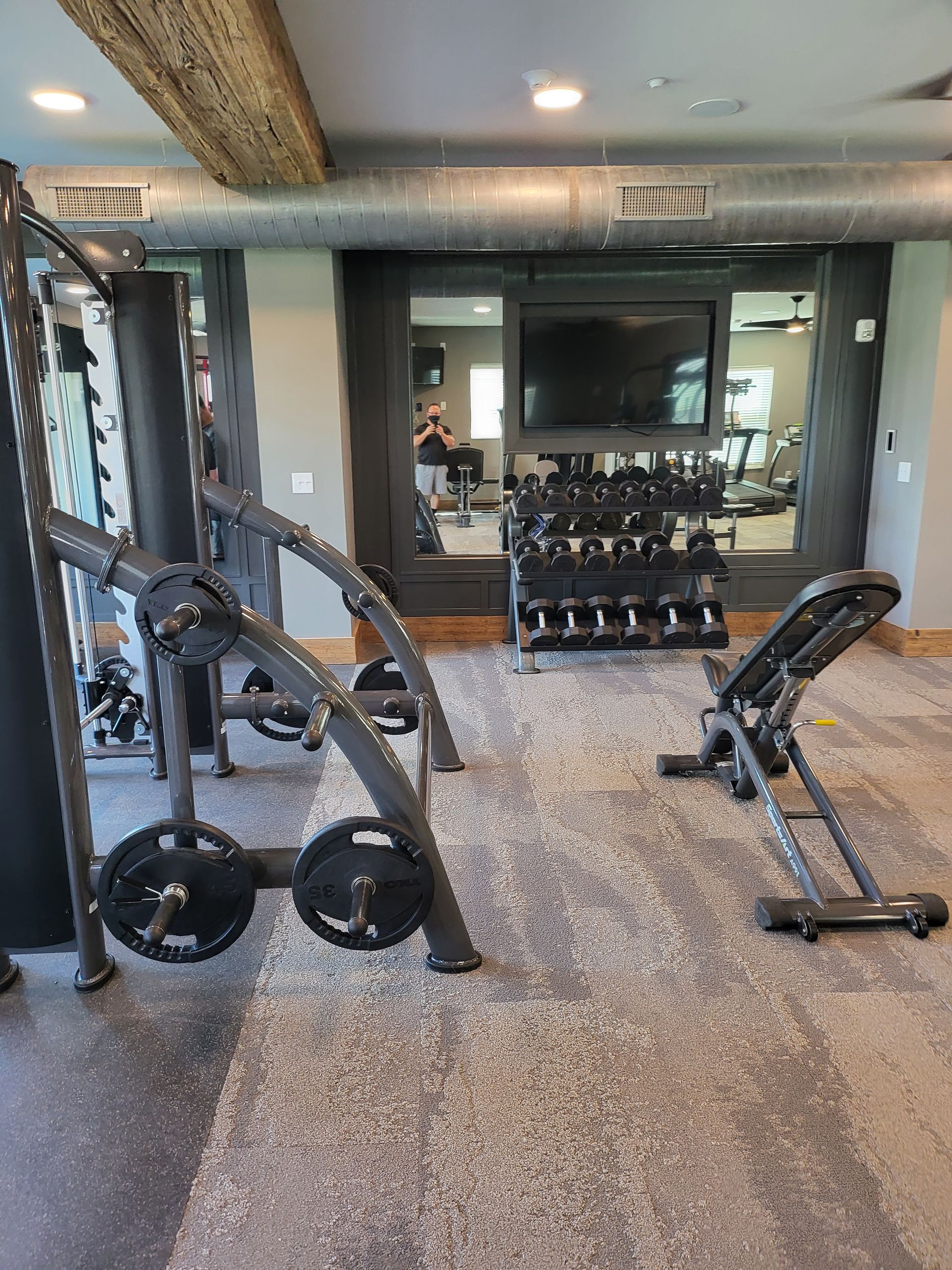 Gym with weight machines, dumbbells, and a mirrored wall on a speckled floor.