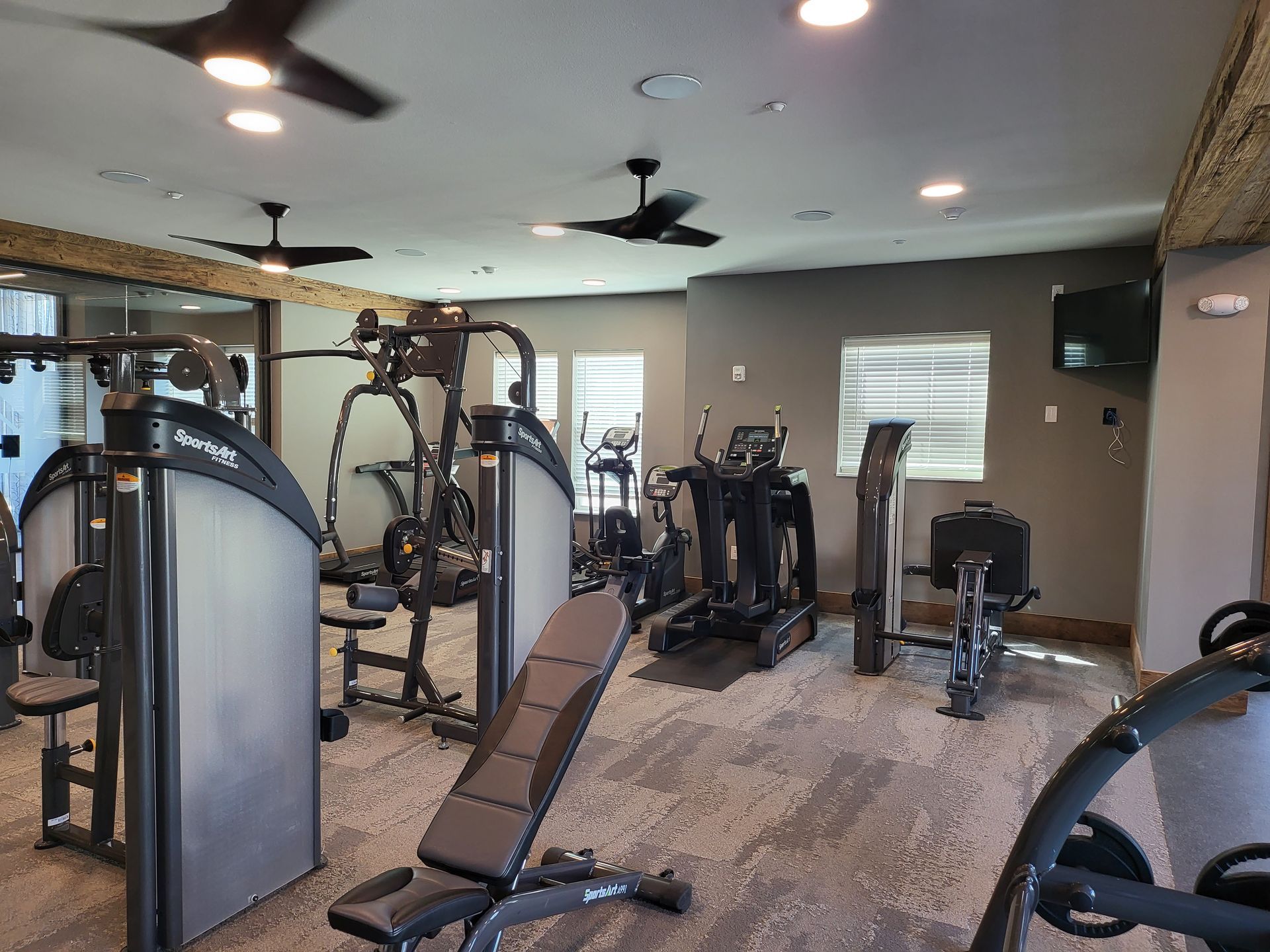 Modern gym interior with weight machines, benches, and ceiling fans on wood flooring