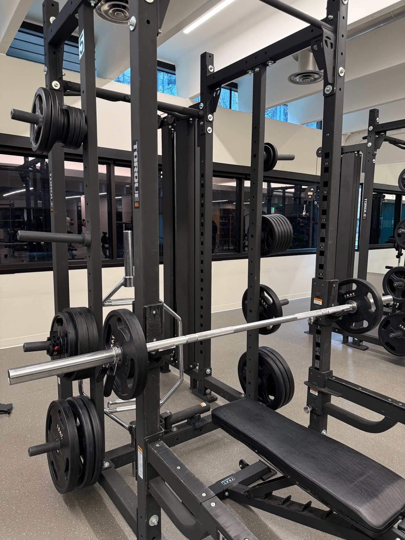 Gym squat rack with barbell, weight plates, and an incline bench in a fitness room