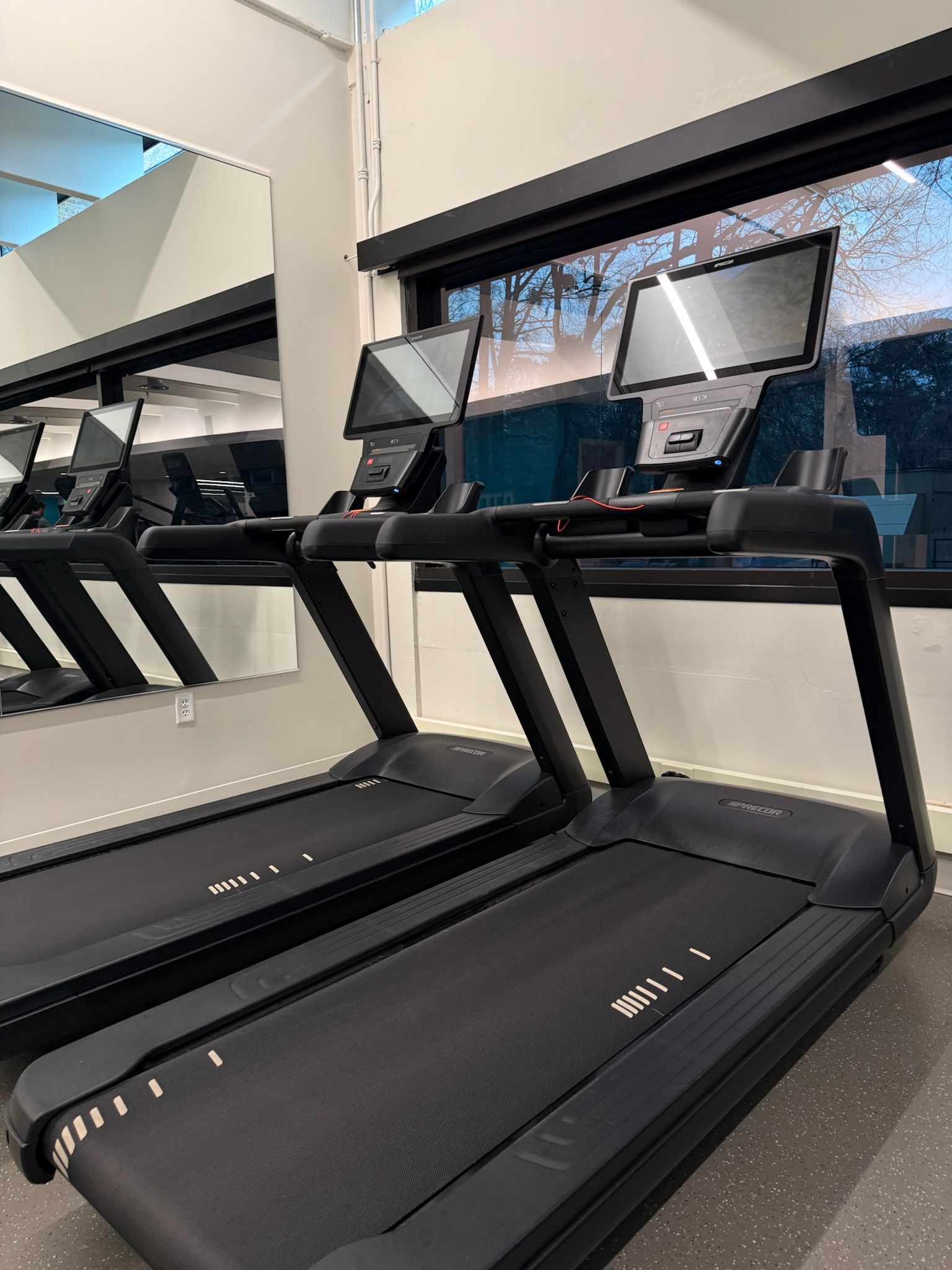 Two treadmills in a gym, with mirrors and console screens behind them.