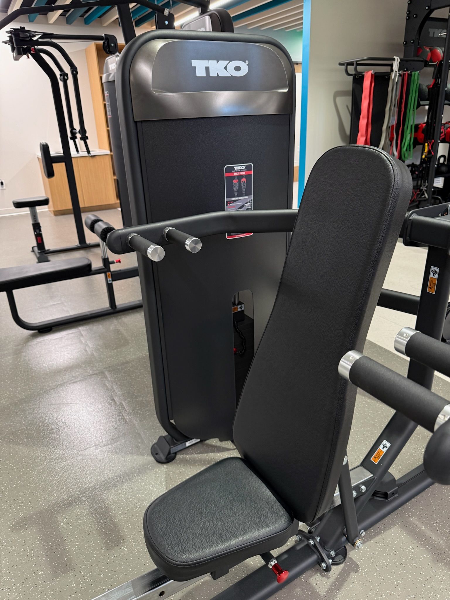 Seated exercise machine in a gym with black padding and gray frame.