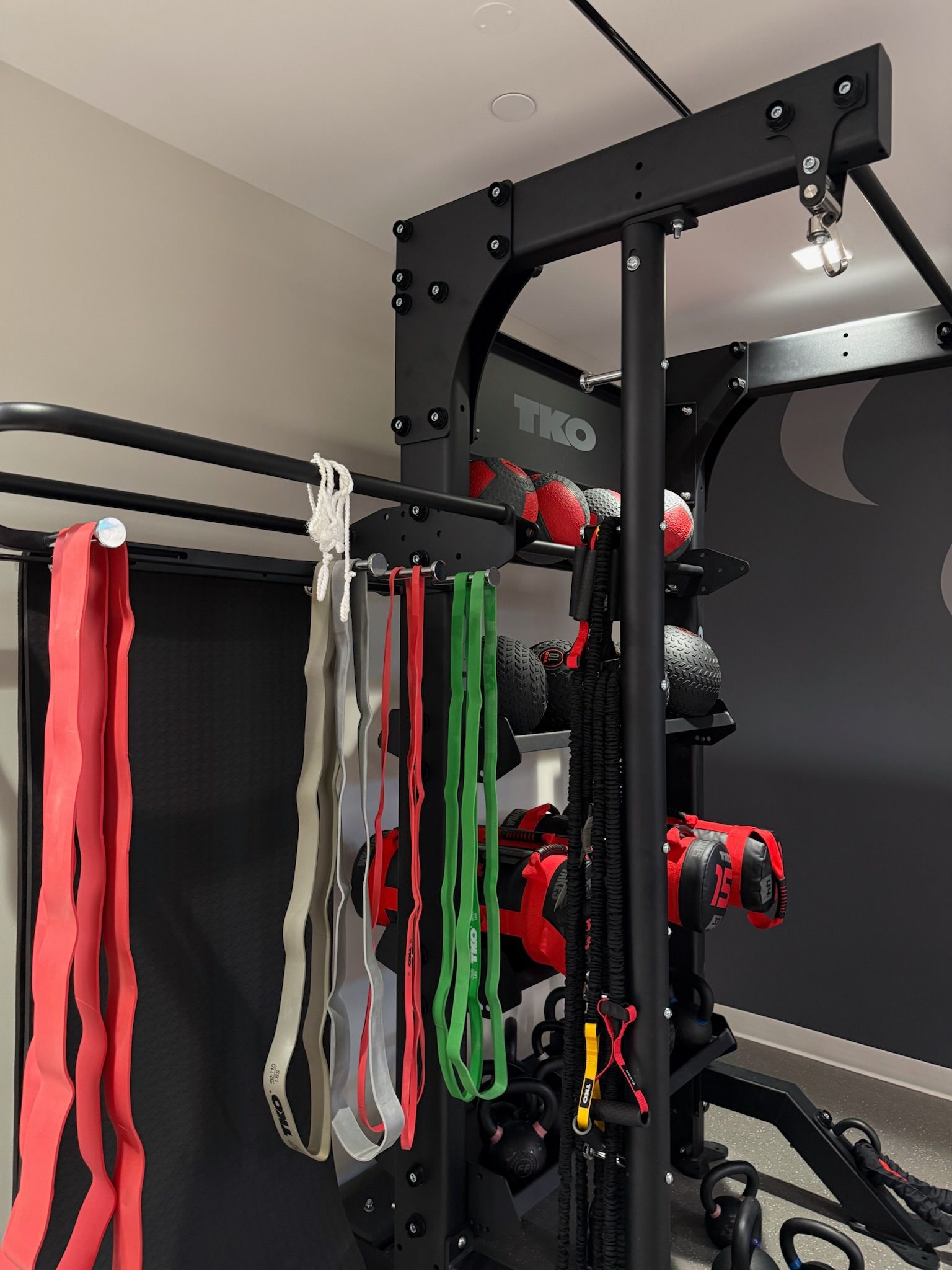 Gym cable machine with hanging resistance bands and red workout accessories, against a dark wall
