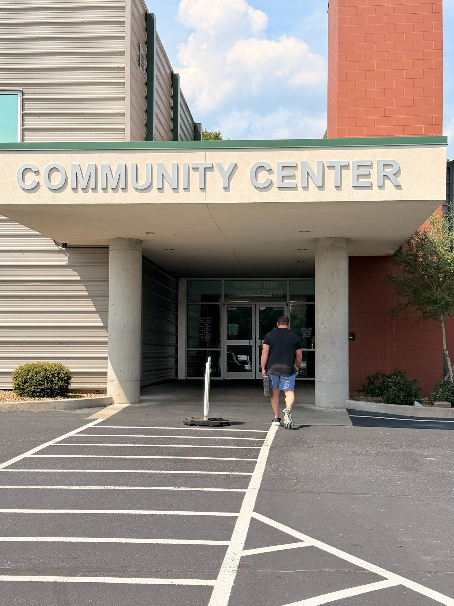 Community center entrance with a person walking in under a sign; striped walkway and brick building facade.