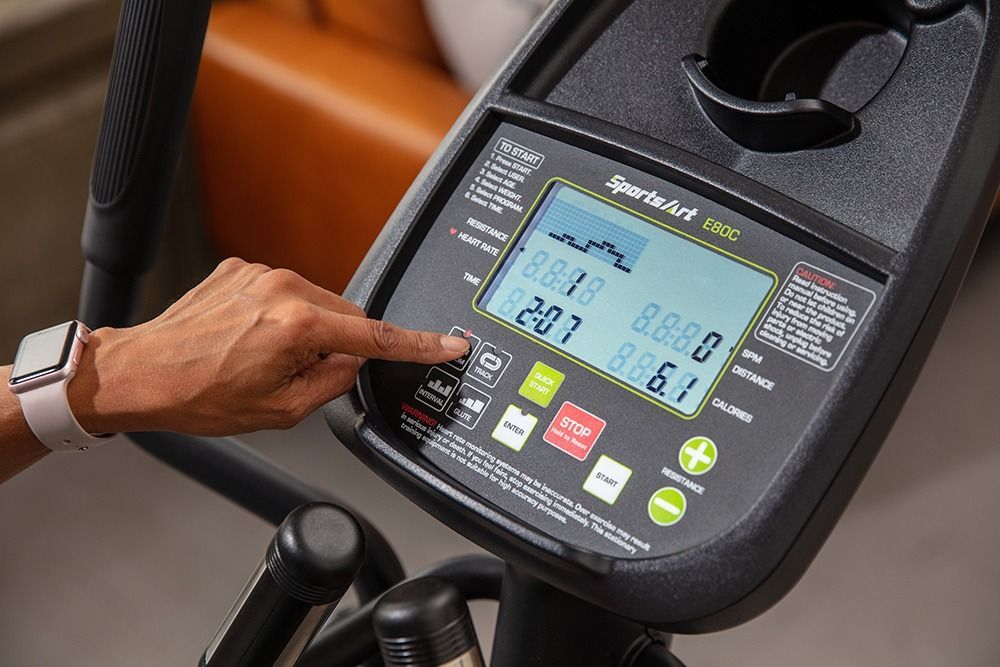 Elliptical machine on a rug in a bright living room with a sofa and large windows