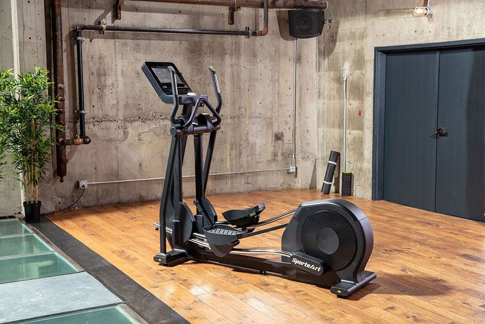 Elliptical machine in a gym with wood flooring, concrete walls, and a blue door.