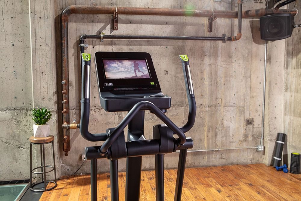 Elliptical machine in a gym with wood flooring, concrete walls, and a blue door.