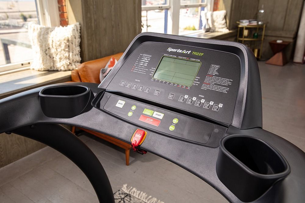 Treadmill in a bright living room beside a couch and large window.