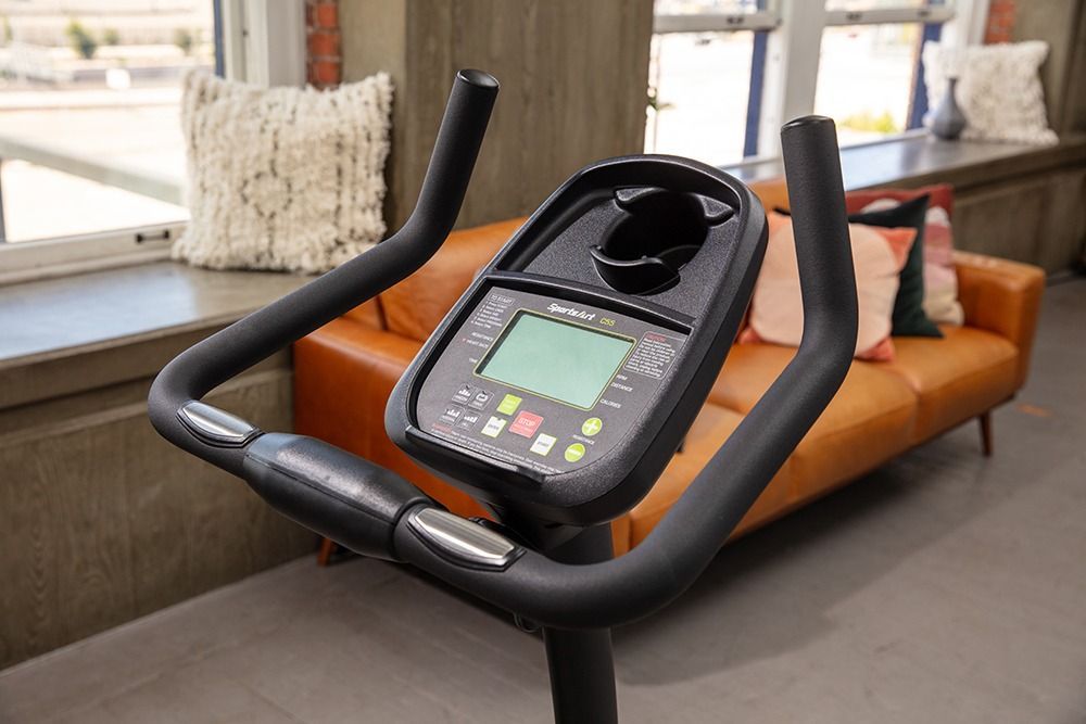 Black stationary exercise bike in a bright living room beside an orange sofa and coffee table.