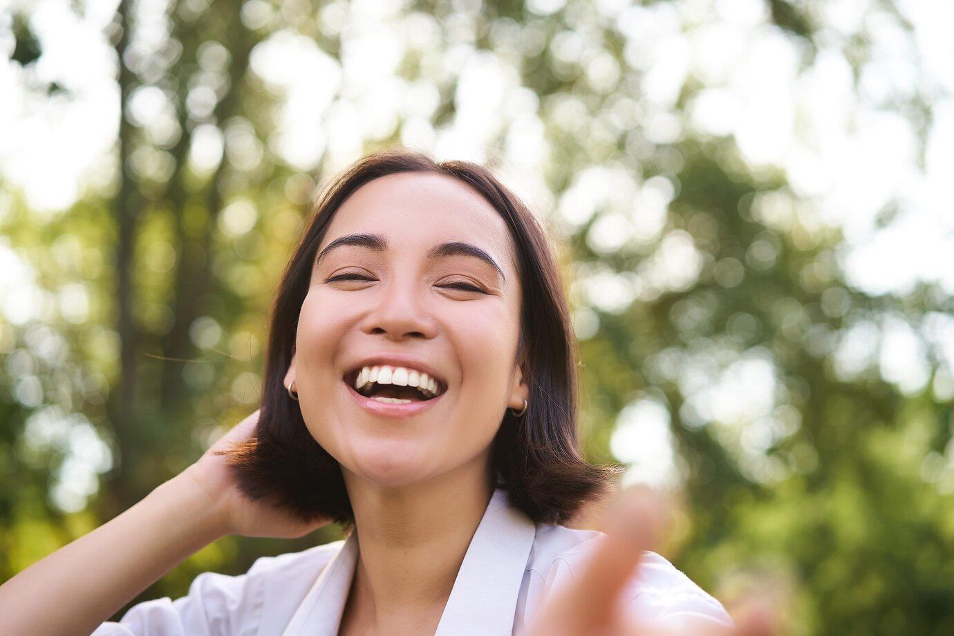 A woman is laughing with her eyes closed and her hand in her hair.