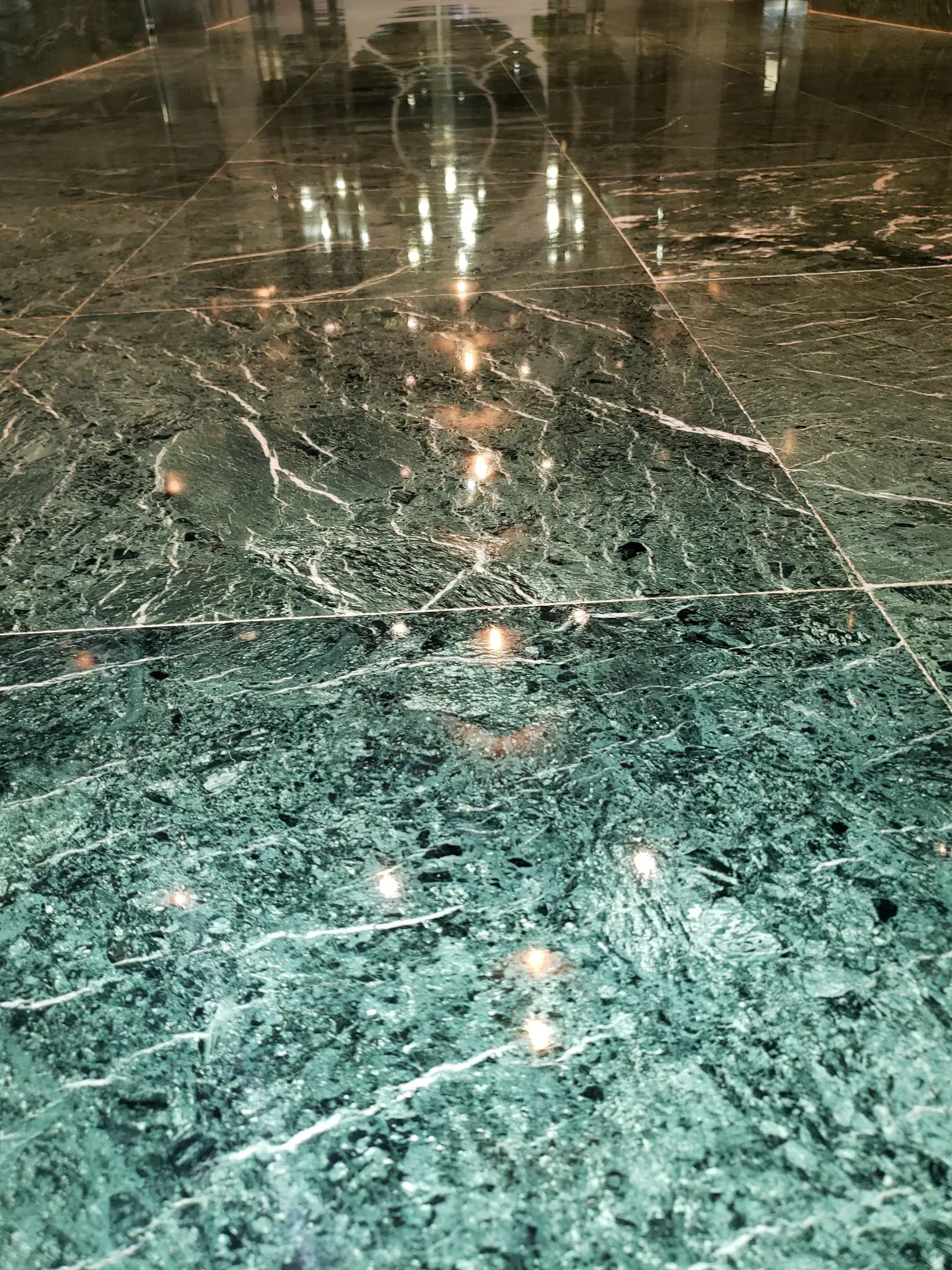 Polished green marble floor with reflections from overhead lights and blurred silhouettes in the distance
