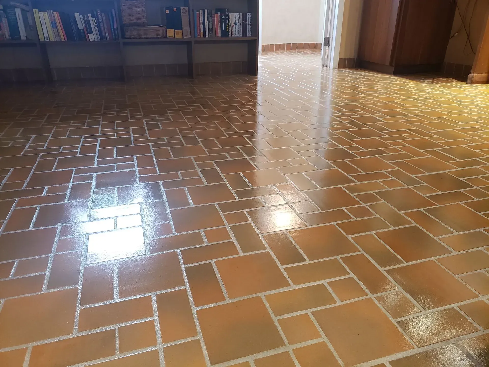 Shiny brown tiled floor with reflections in a room, bookshelves along the back wall.