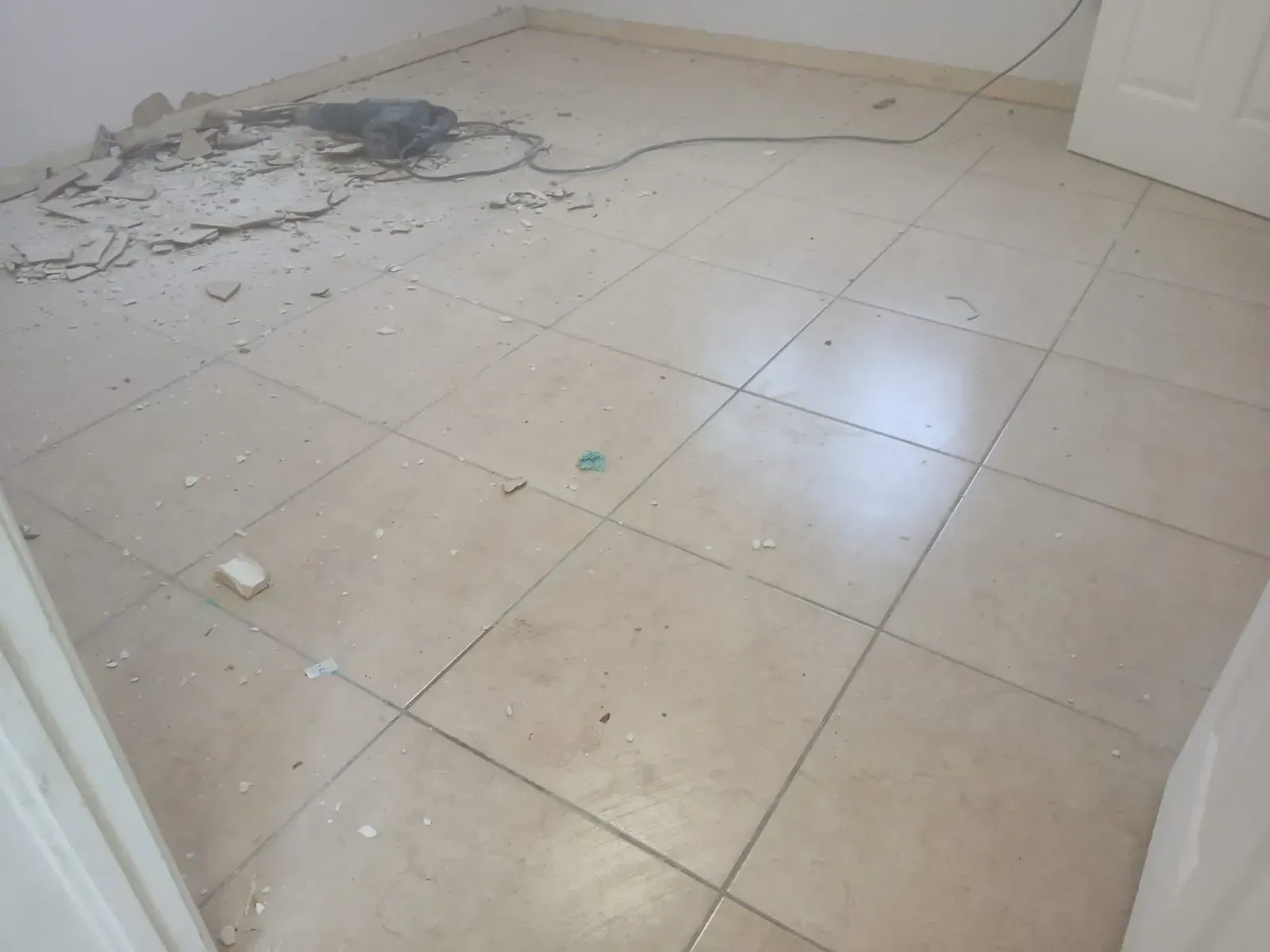 Damaged tiled floor with debris and cracked plaster near a wall corner