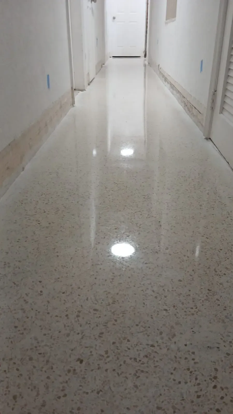Empty polished hallway with white walls and bright ceiling lights reflecting on the floor