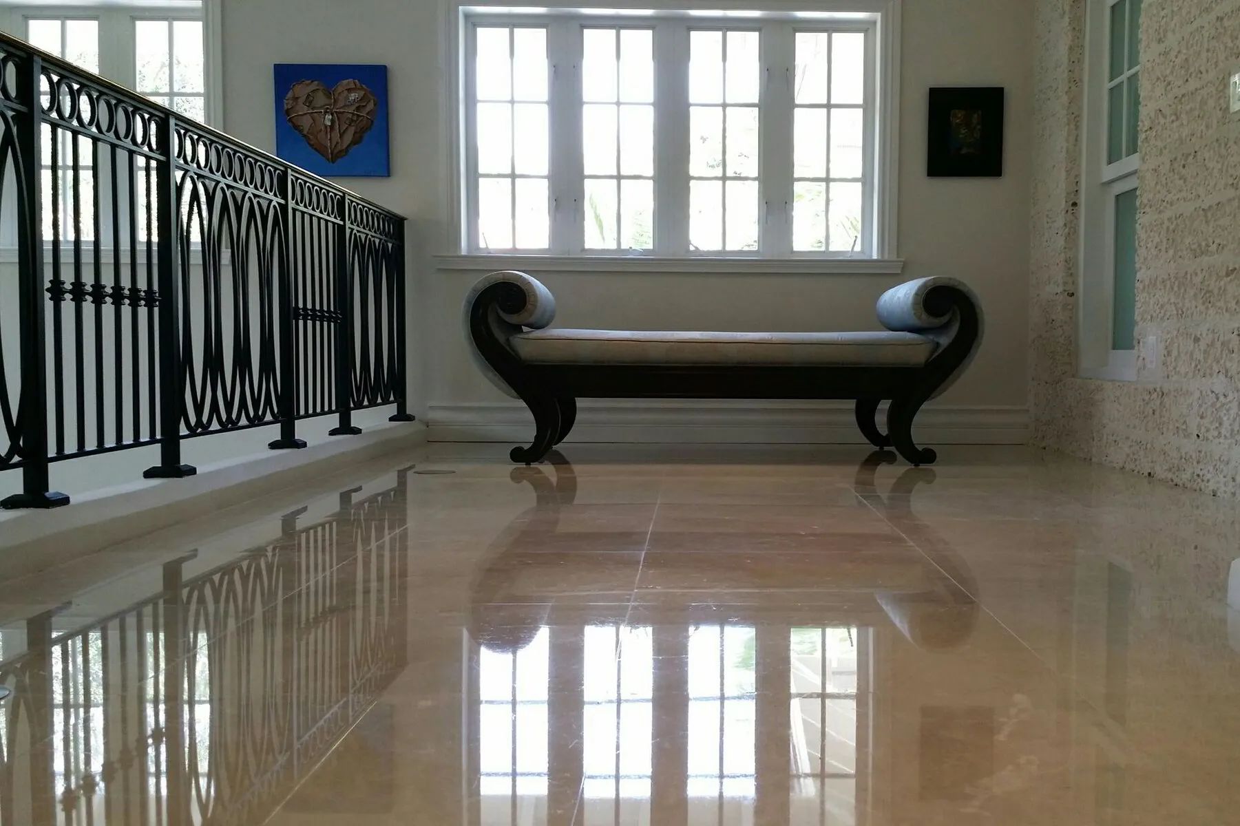Elegant hallway with a bench, ornate railing, and a bright window reflection on polished marble floor