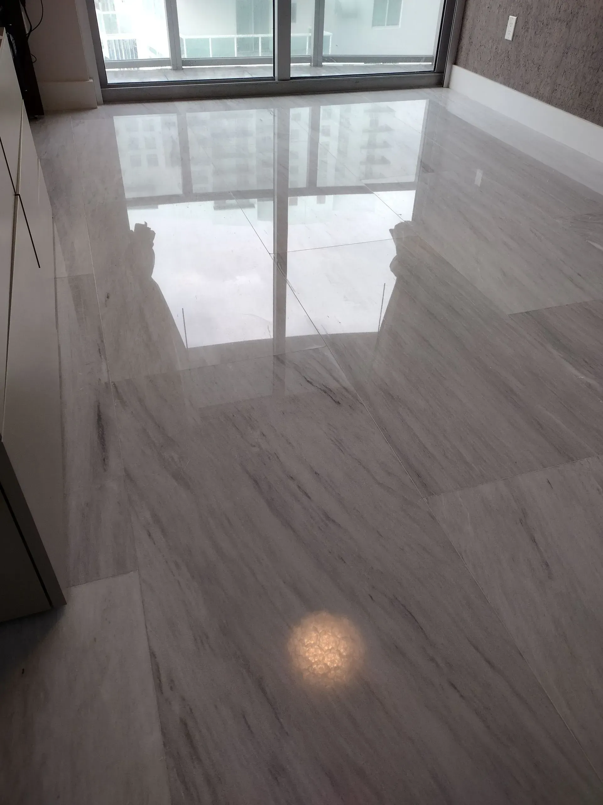 Empty polished floor reflecting light in a room with large windows.