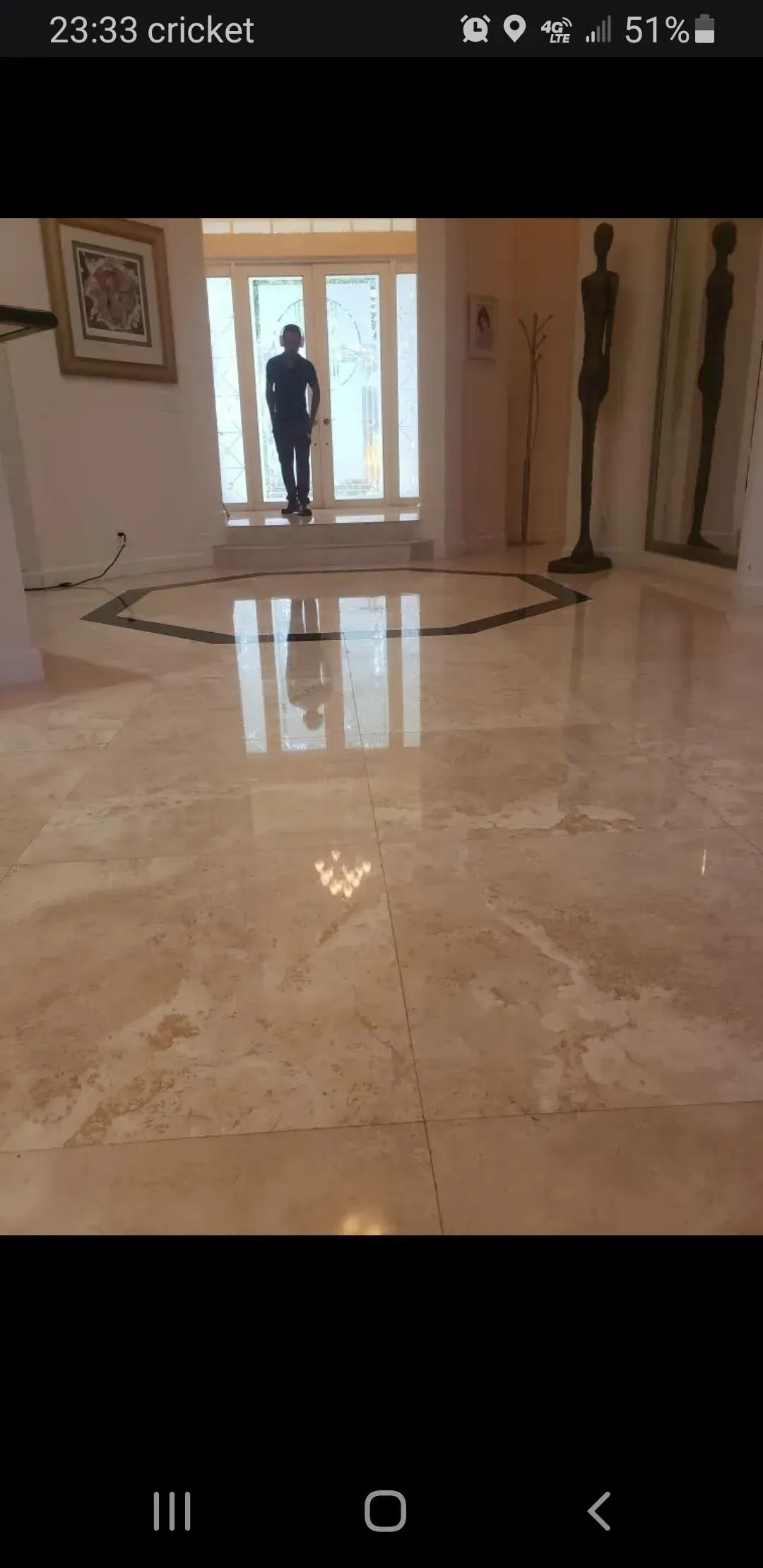 Large marble-floored lobby with a person silhouetted at the glass entrance and statues along the walls.