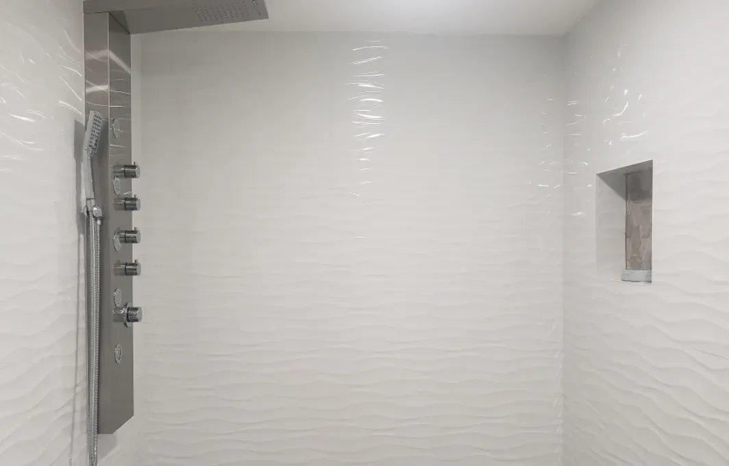 Modern white shower with tiled walls, multiple wall-mounted controls, and a recessed niche.