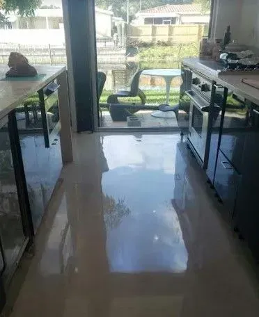 Indoor room with glossy tiled floor, tables on both sides, and a view through an open doorway to outside greenery.