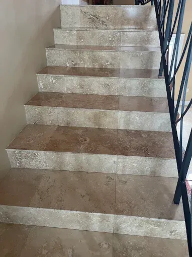 Indoor staircase with beige steps and a black metal railing on the right.