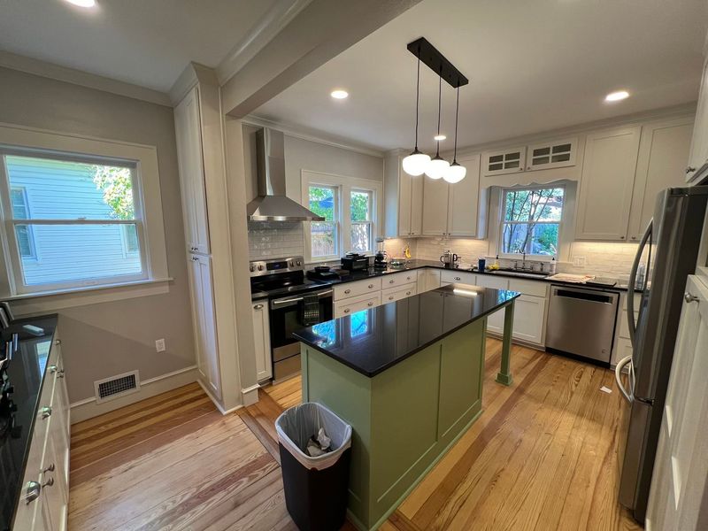 Bright kitchen with green island, black countertops, white cabinets, and hardwood floors.