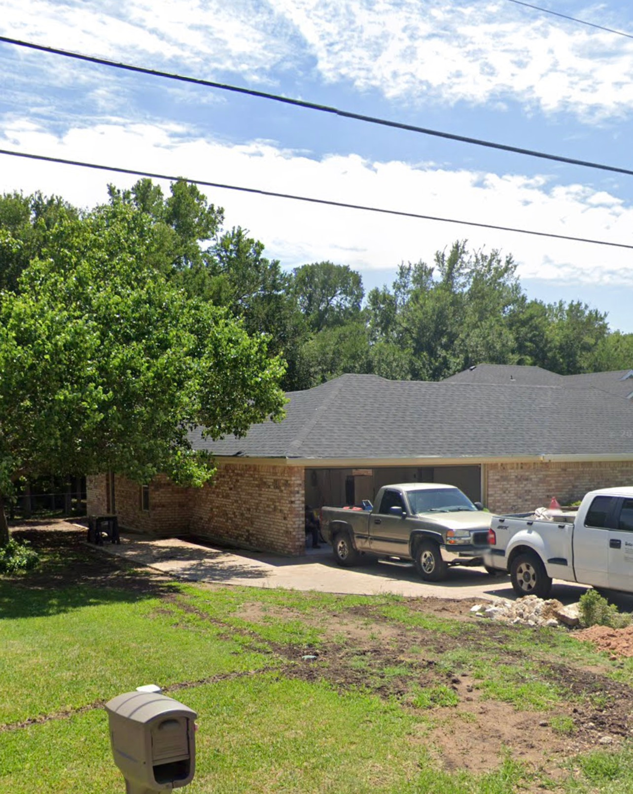Suburban house with two parked pickup trucks, green lawn, and power lines under a blue sky