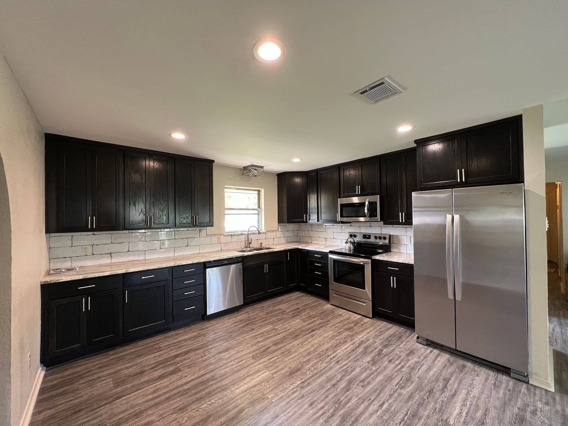 Modern kitchen with dark cabinets, stainless steel appliances, and light stone backsplash
