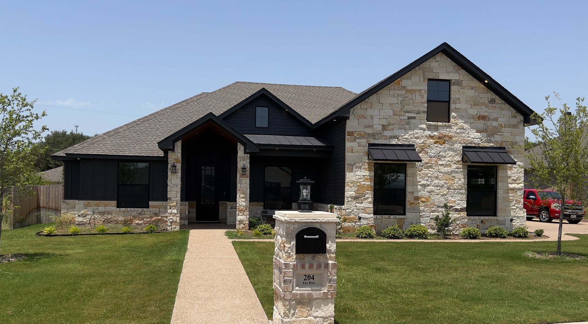 Modern stone and dark-gray house with a front lawn and mailbox under a clear sky